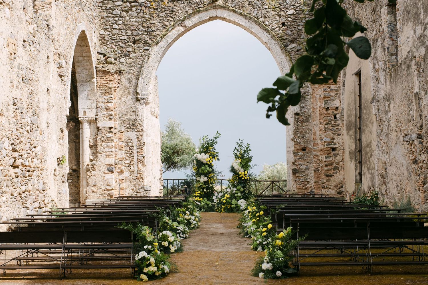 Ancient stone ruins of a medieval church with arched windows and doorways stand against a bright sky.