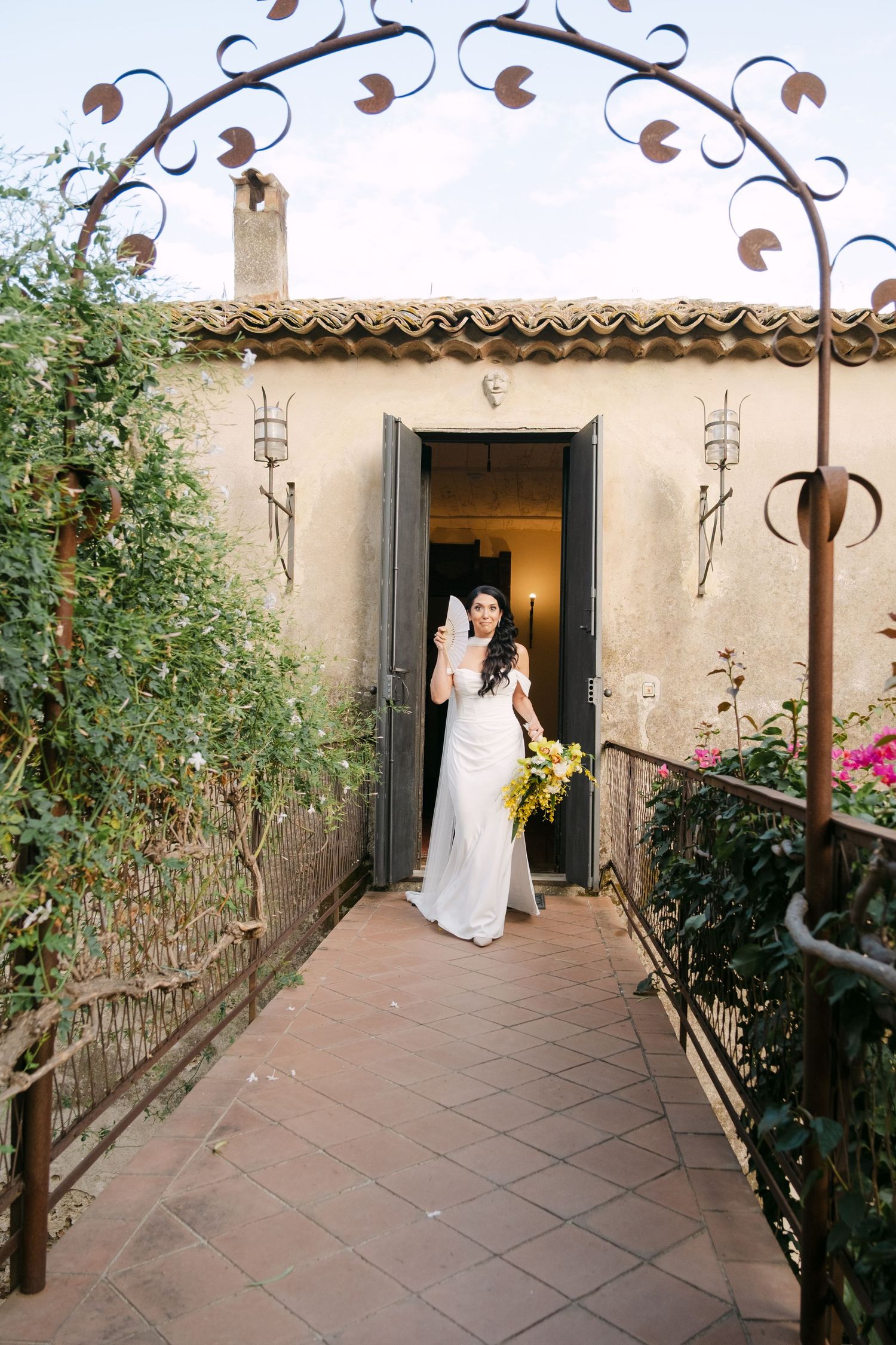 A wedding scene unfolds on a Spanish-style terrace with wrought iron details and terra cotta tiles.