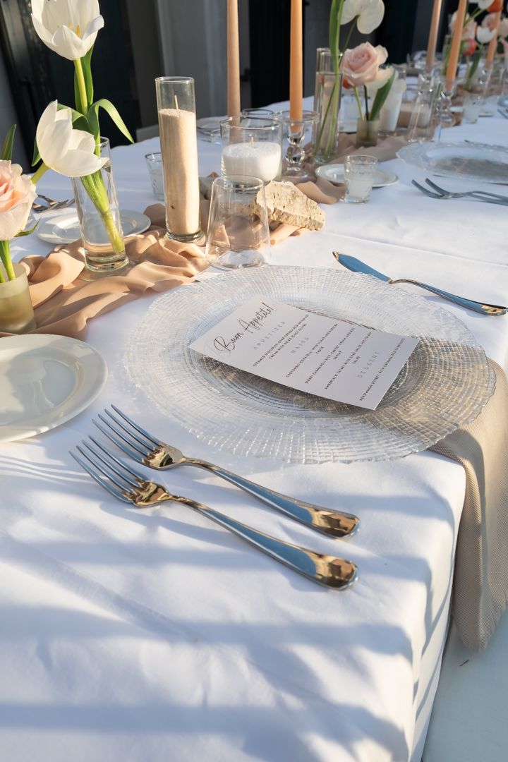 Elegant table setting with white linens, gold cutlery, and menu cards decorated with delicate floral centerpieces.