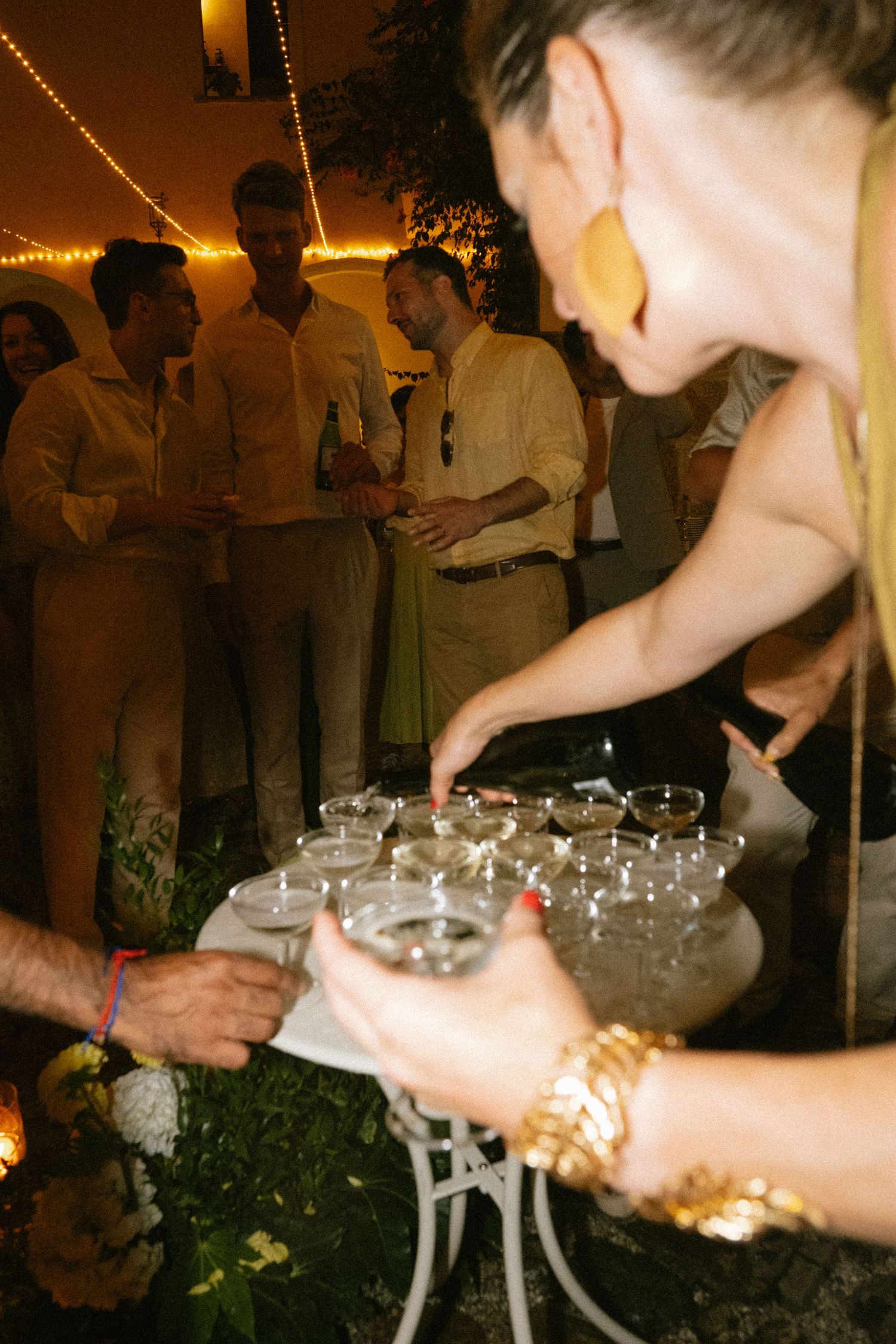 Hands arranging champagne glasses for a wedding toast under ambient lighting.