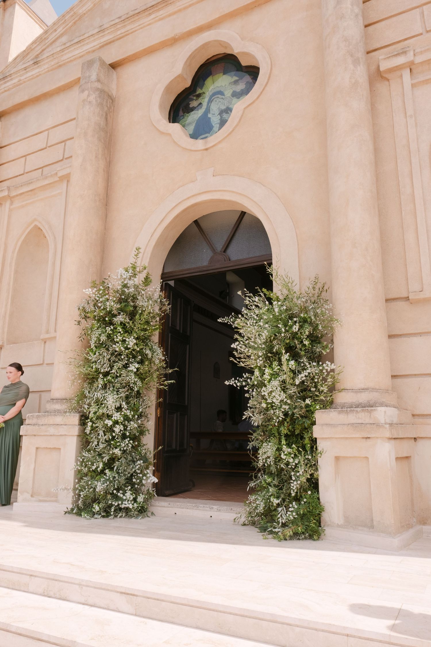 Mediterranean style church entrance decorated with olive trees and greenery.