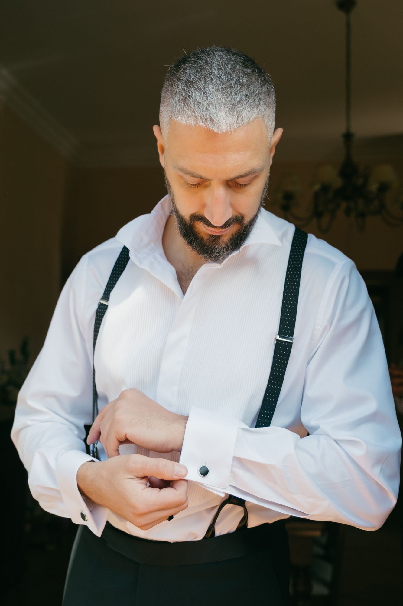 Person in a white dress shirt and black suspenders adjusts their cuff links in a sequence of photos.