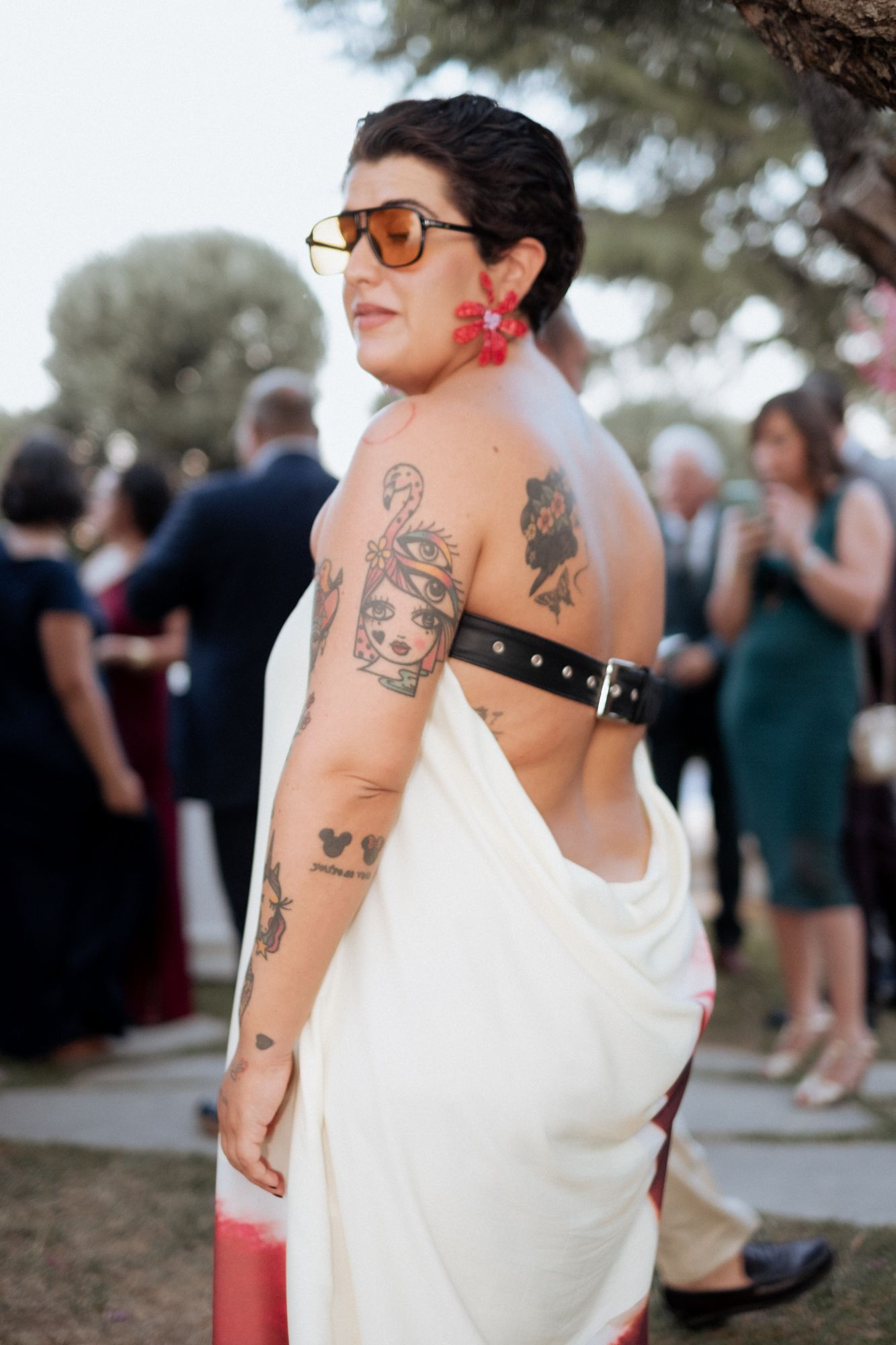 Artistic detail shots of tattoos and white dress at outdoor wedding gathering.