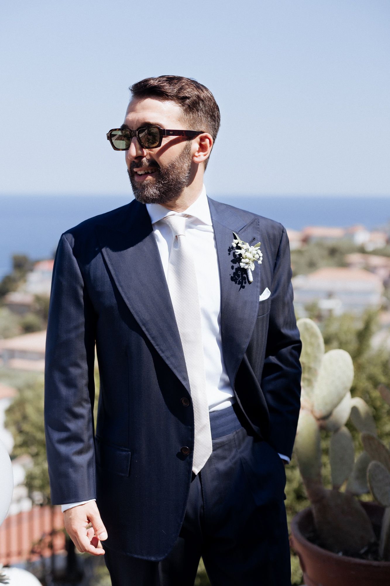 Groom in a classic navy suit and white tie poses against a scenic outdoor backdrop.