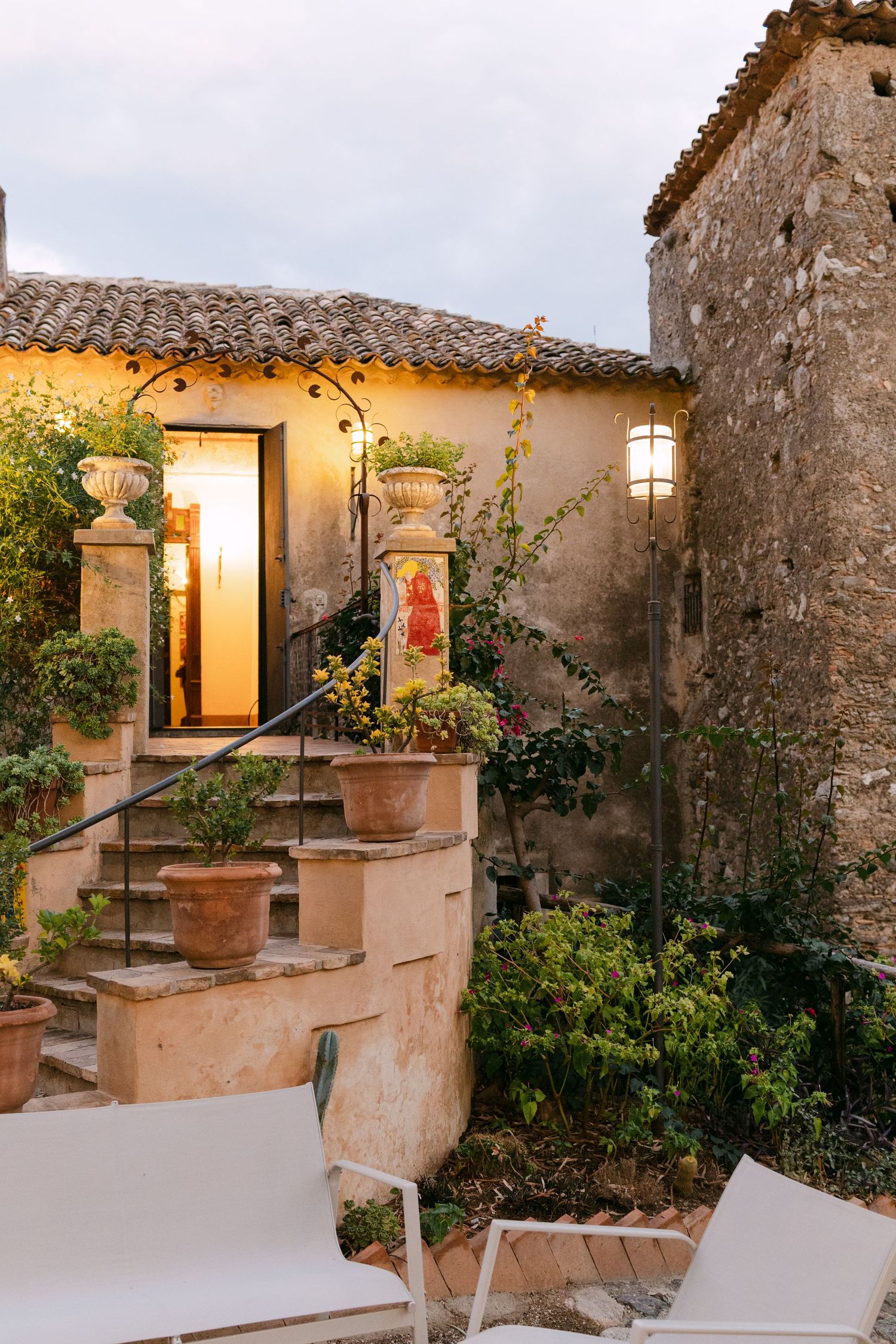 Stone terrace with illuminated lanterns and white lounge chairs at dusk.