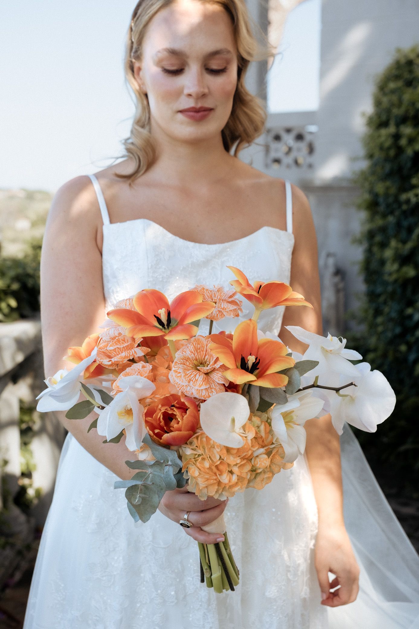 Bridal bouquet featuring orange lilies, white orchids and eucalyptus leaves against a white dress.