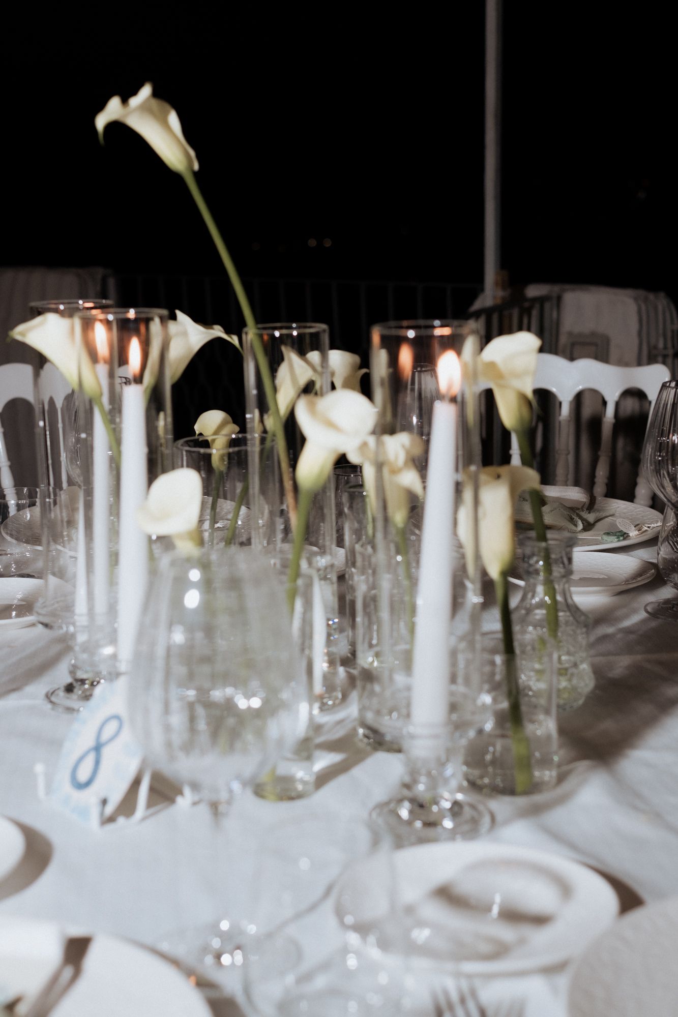 Elegant table setting with white calla lilies in tall glass vases and candlelight for a wedding reception.