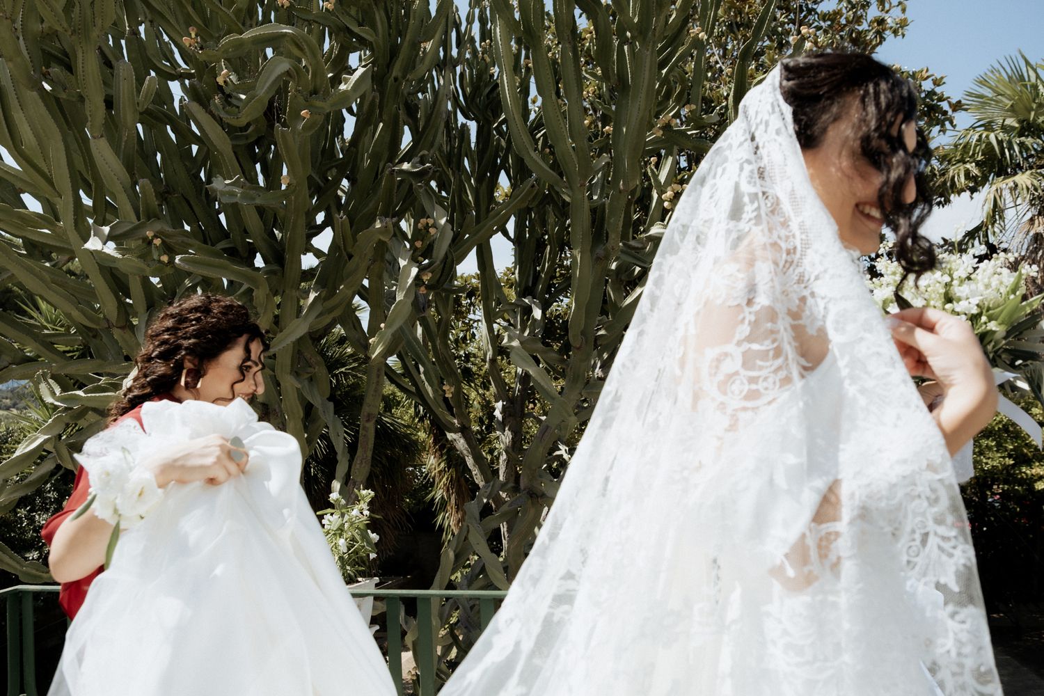 A bride in a flowing white lace wedding dress poses outdoors against a natural backdrop.