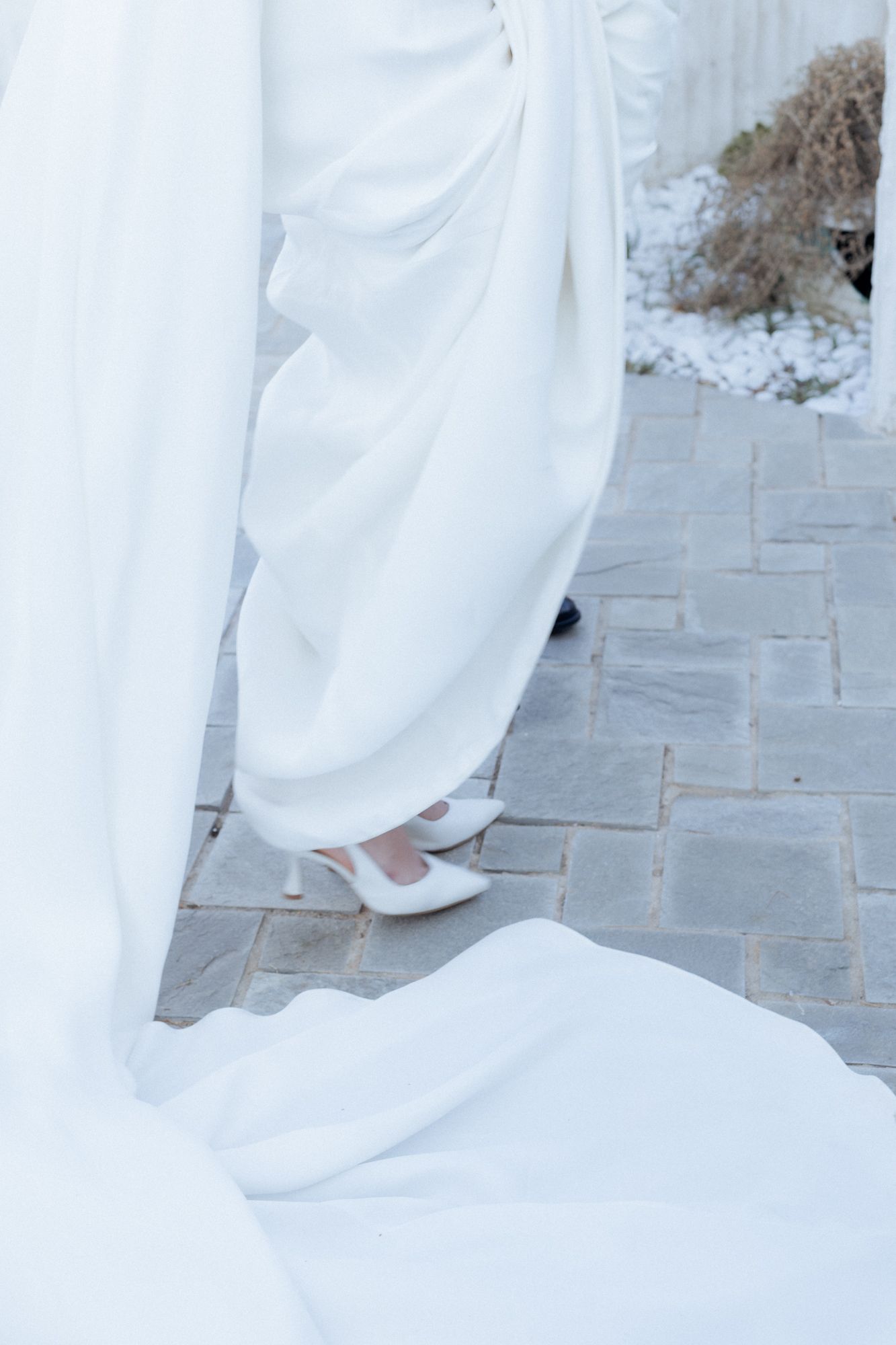 Close-up of white wedding dress hem and bridal shoes on stone paving.