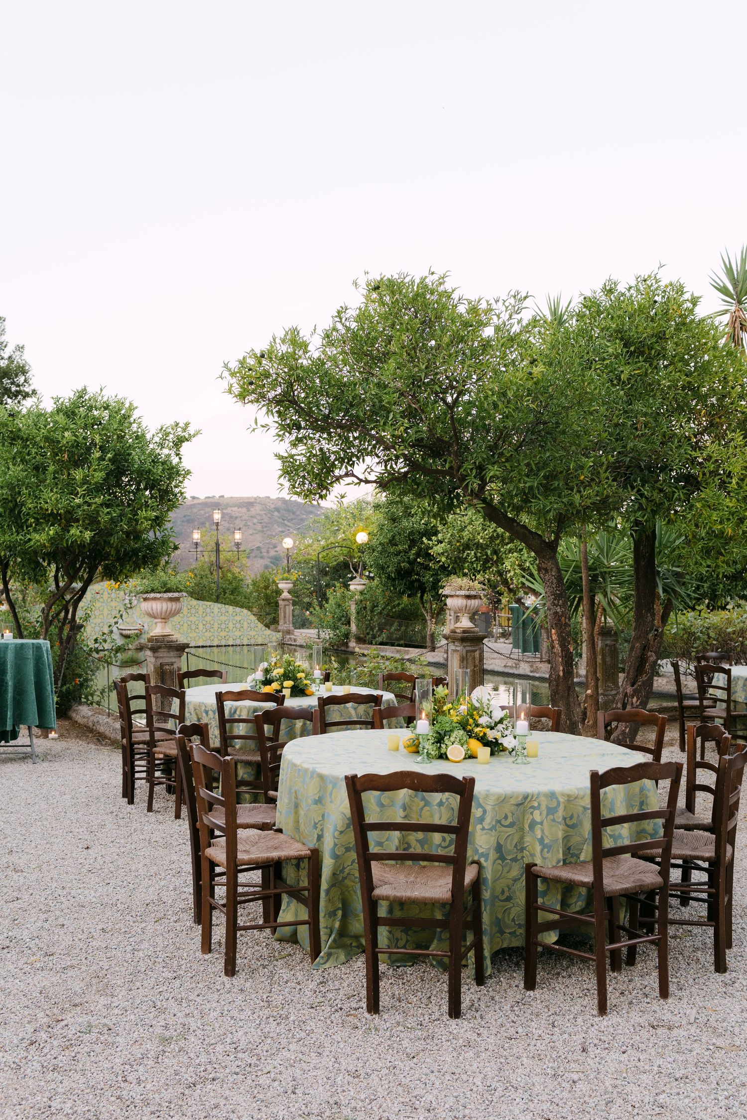 Rustic outdoor wedding reception setup with wooden chairs and tables on gravel patio.
