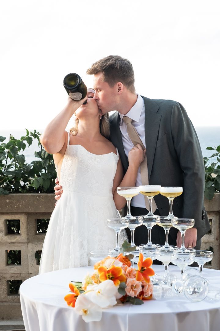 Elegant wedding reception setup with champagne tower and orange floral arrangements by the ocean.