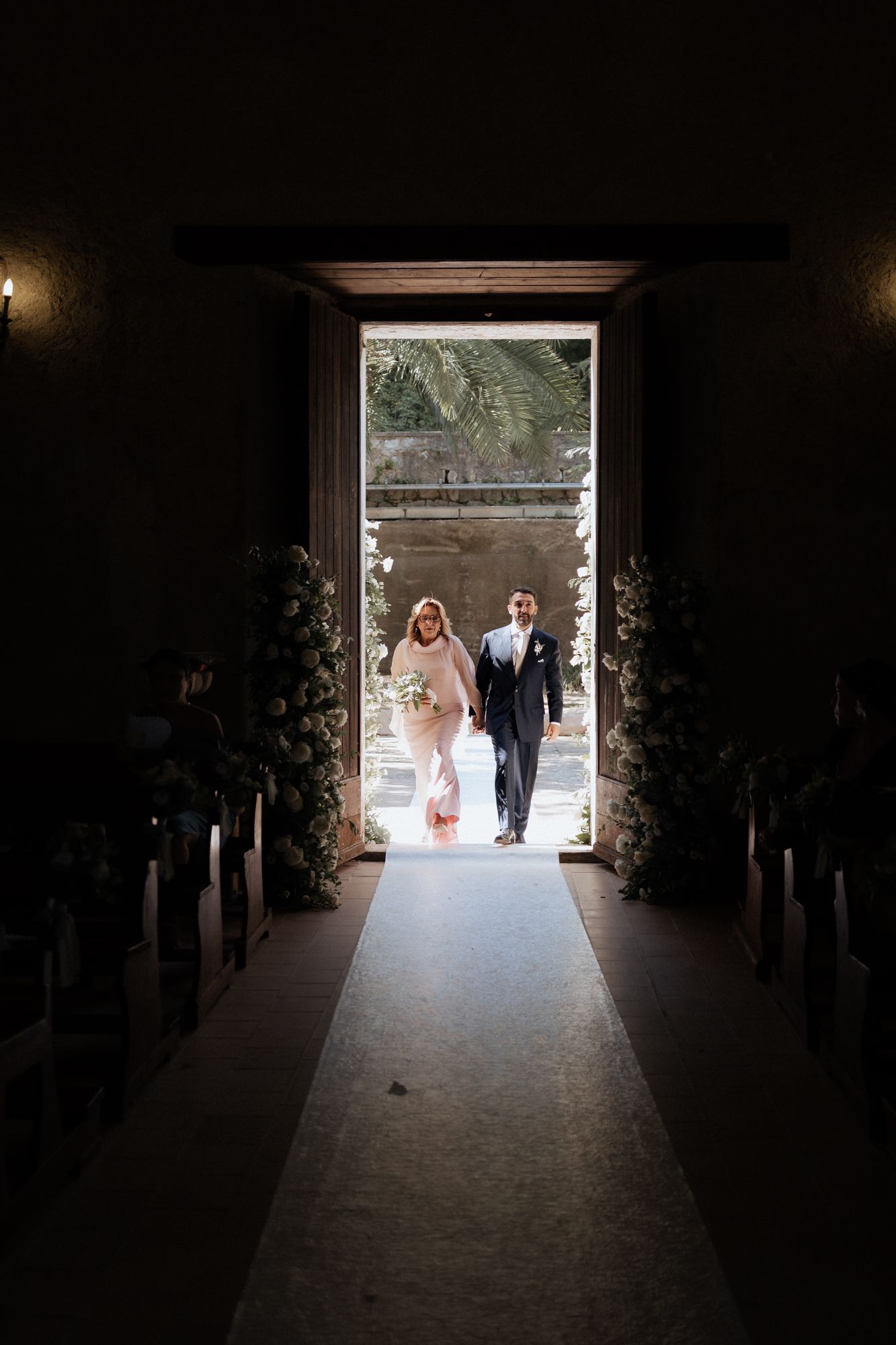 Wedding ceremony silhouette through dark tunnel entrance with bright outdoor light.