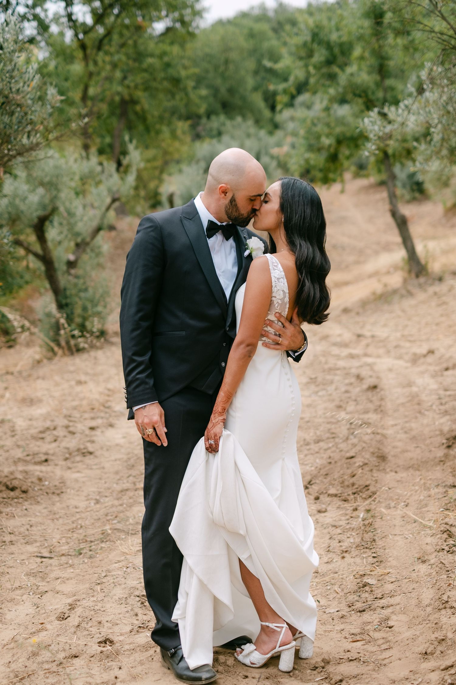 Romantic moment captured in an olive grove with elegant wedding attire.