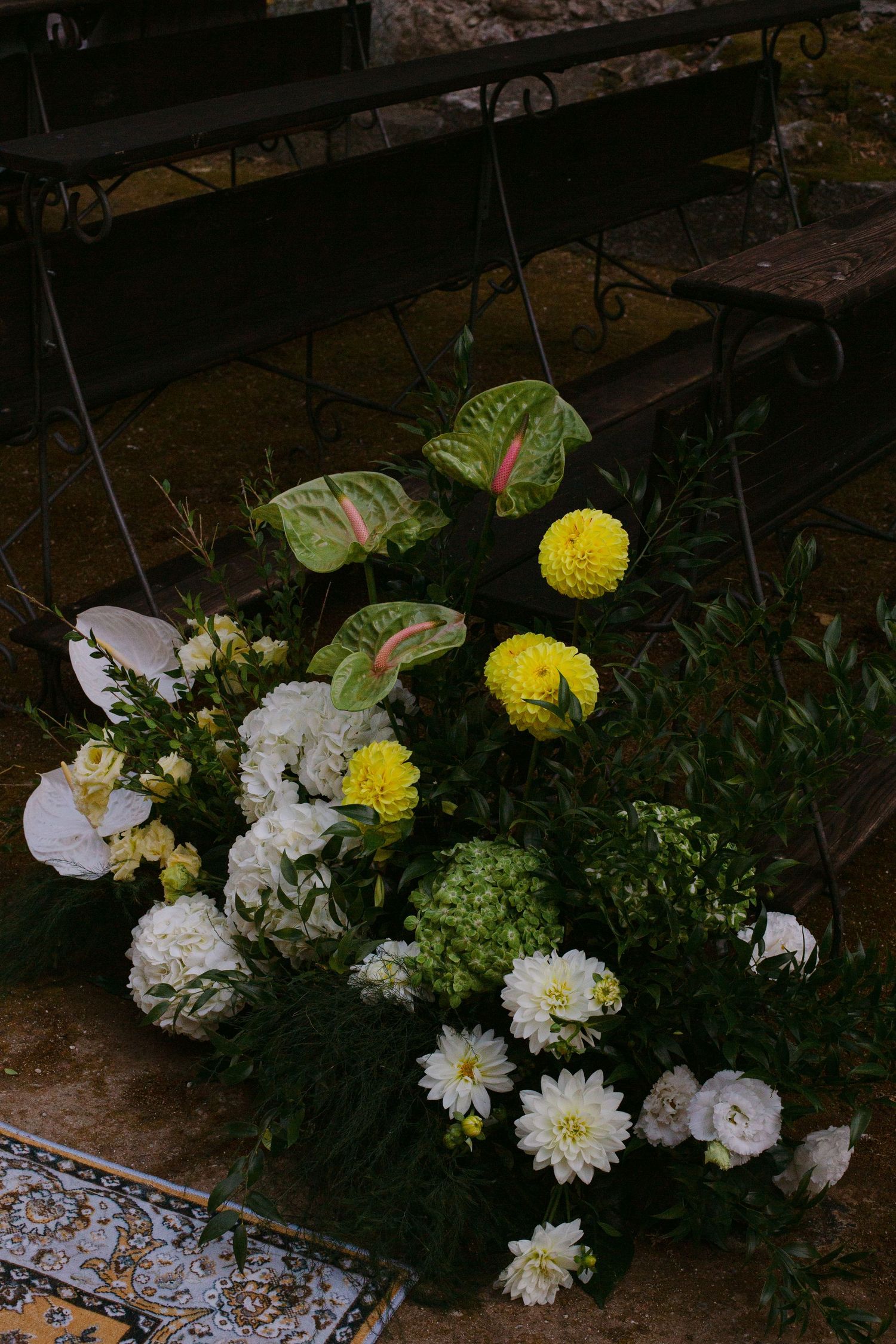 White and yellow floral arrangements with green foliage decorate wooden benches in a rustic setting.