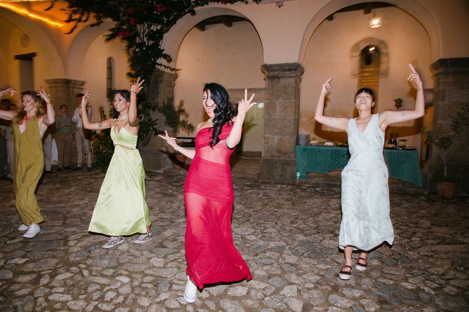 Wedding guests dancing and jumping joyfully on a rustic stone patio at night.