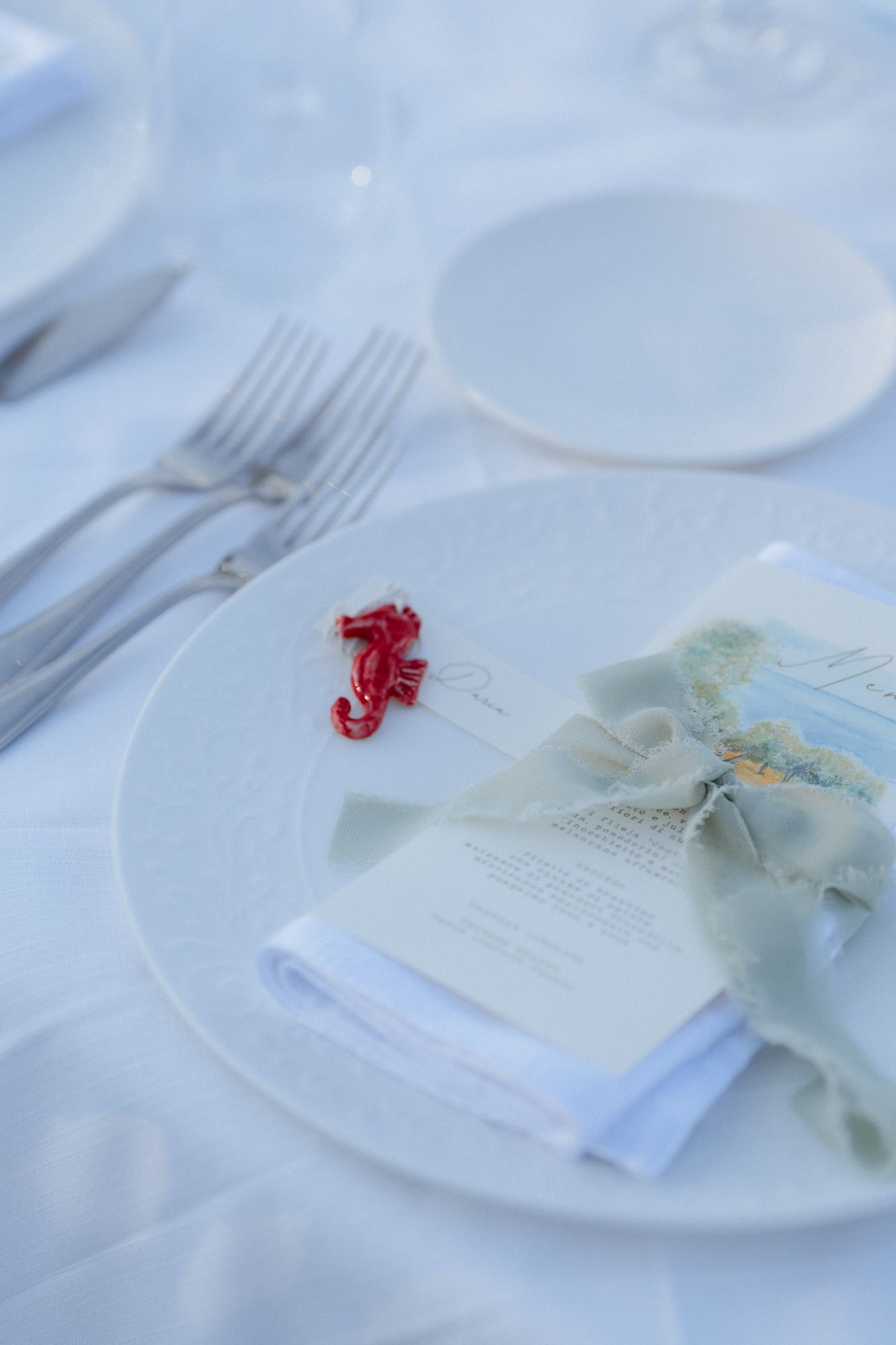 Elegant place setting with white plates and delicate menu cards on a crisp tablecloth.