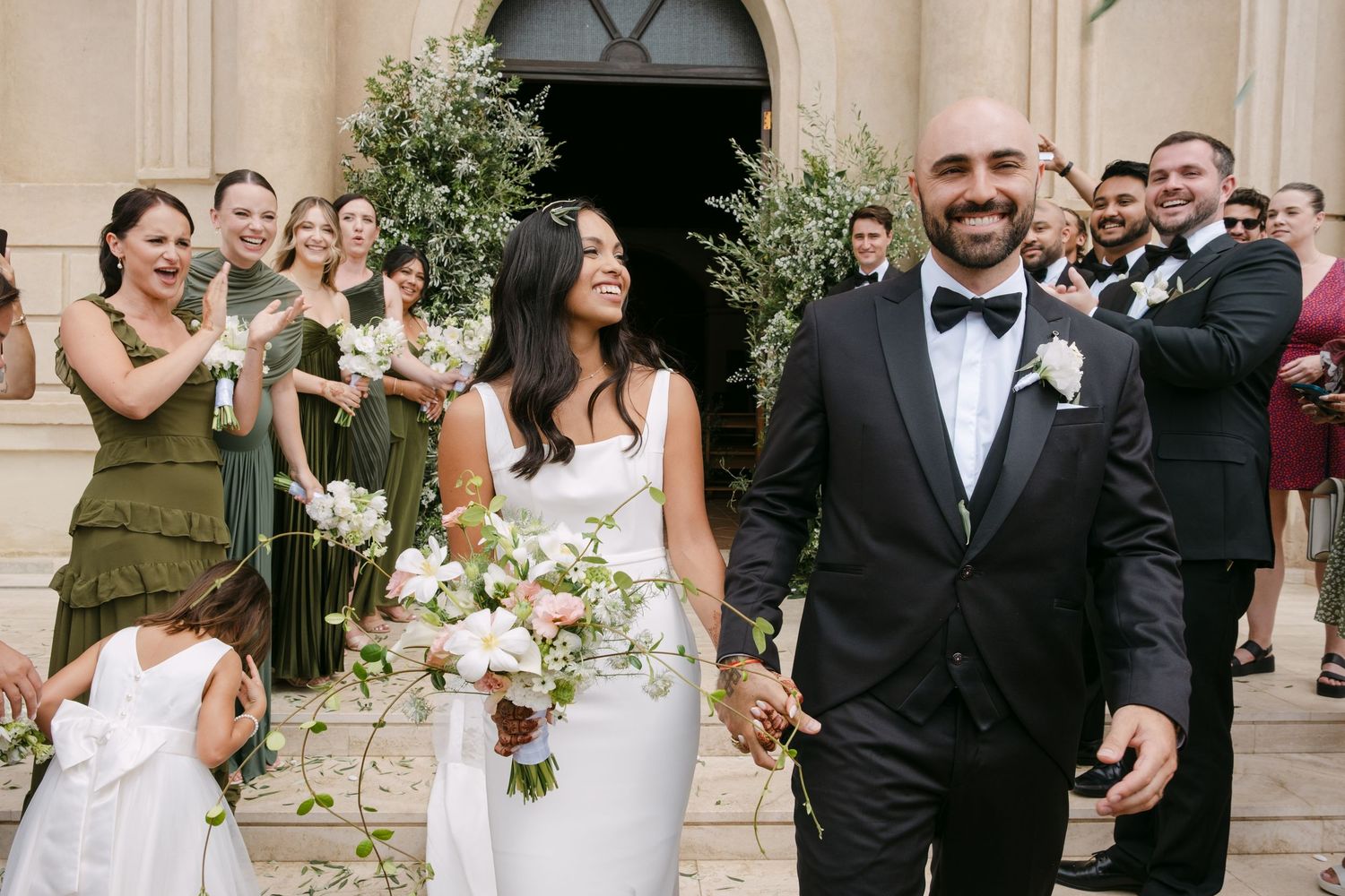 Wedding party celebrating with joy and laughter outside a grand venue with elegant decor and floral arrangements.