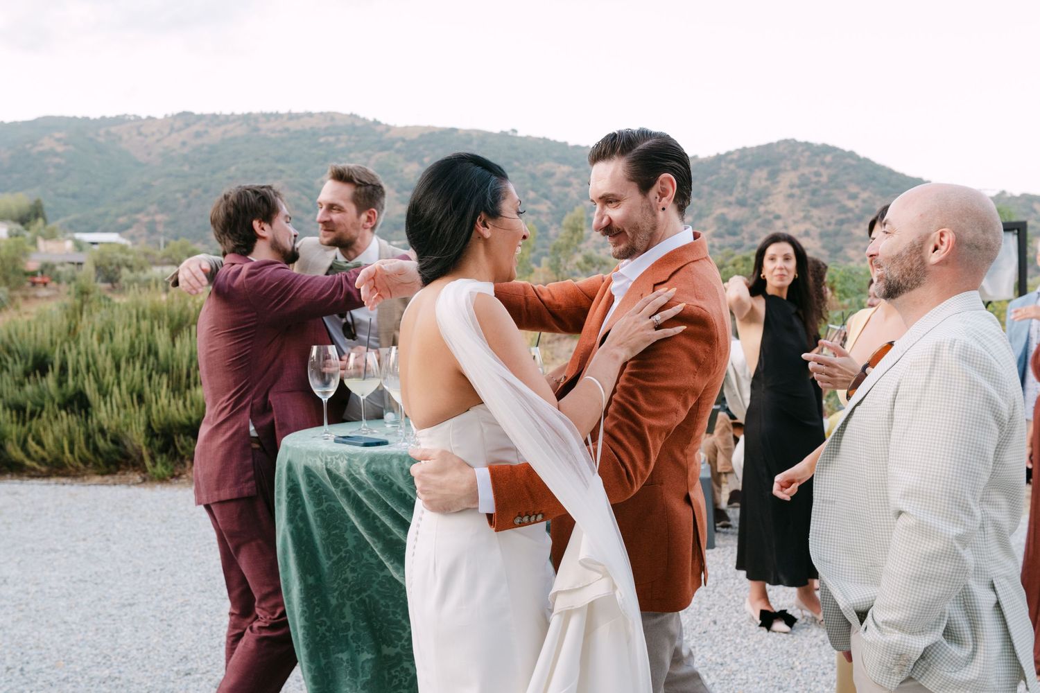 Wedding party celebrates with hugs and embraces against a scenic mountain backdrop.