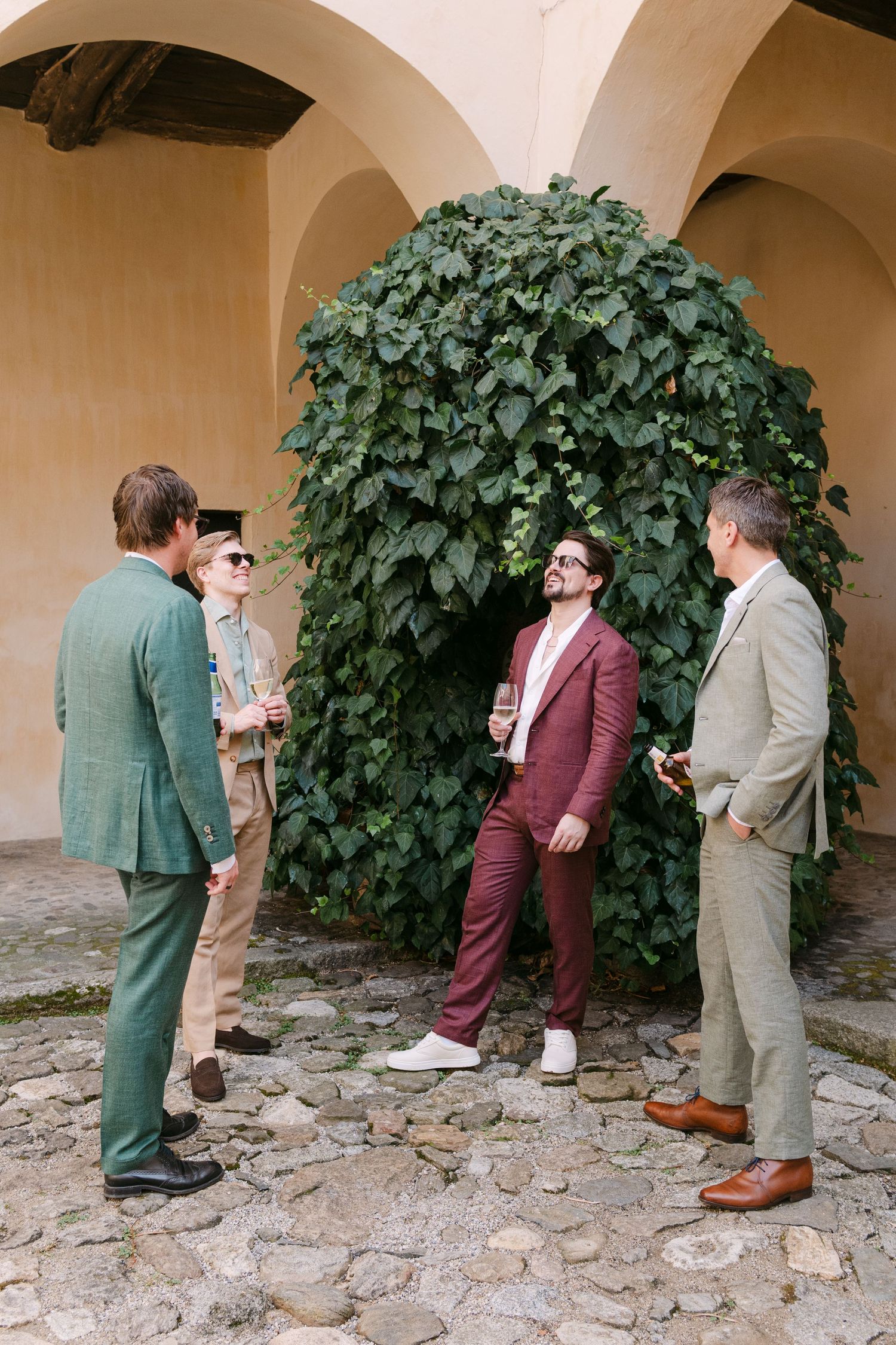 People gathered under stone archways next to lush green vines during an outdoor event.