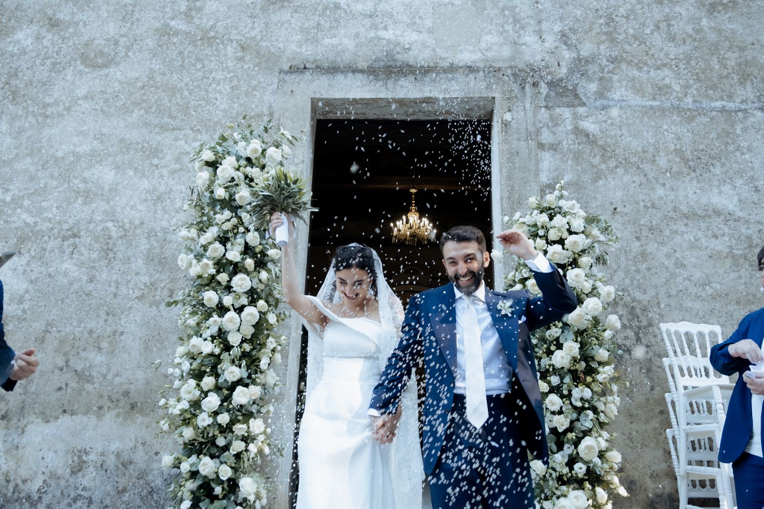 Wedding celebration with white floral arrangements and confetti toss outdoors.