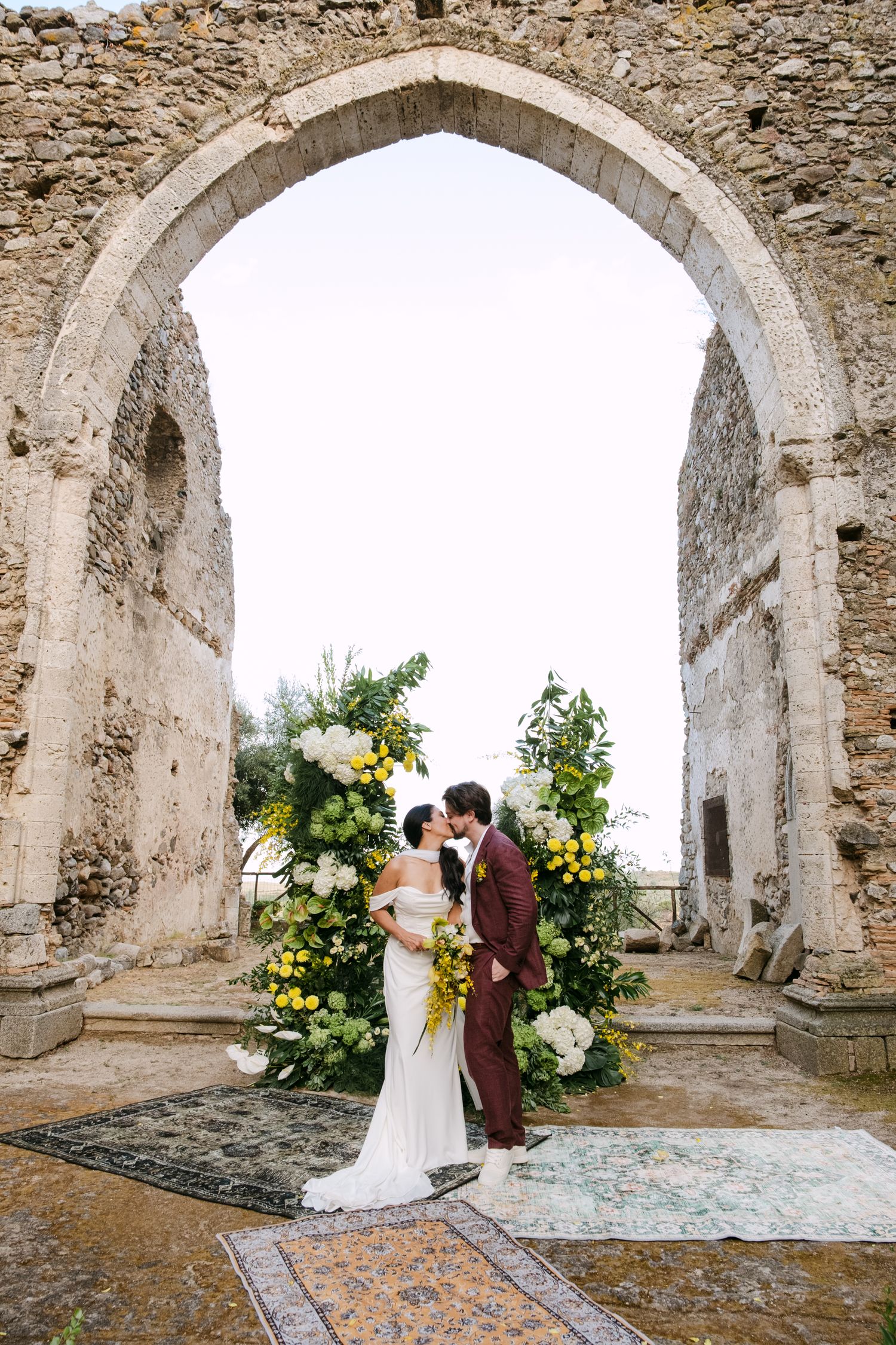A wedding ceremony setup in ancient stone ruins with floral arrangements and arched doorways.