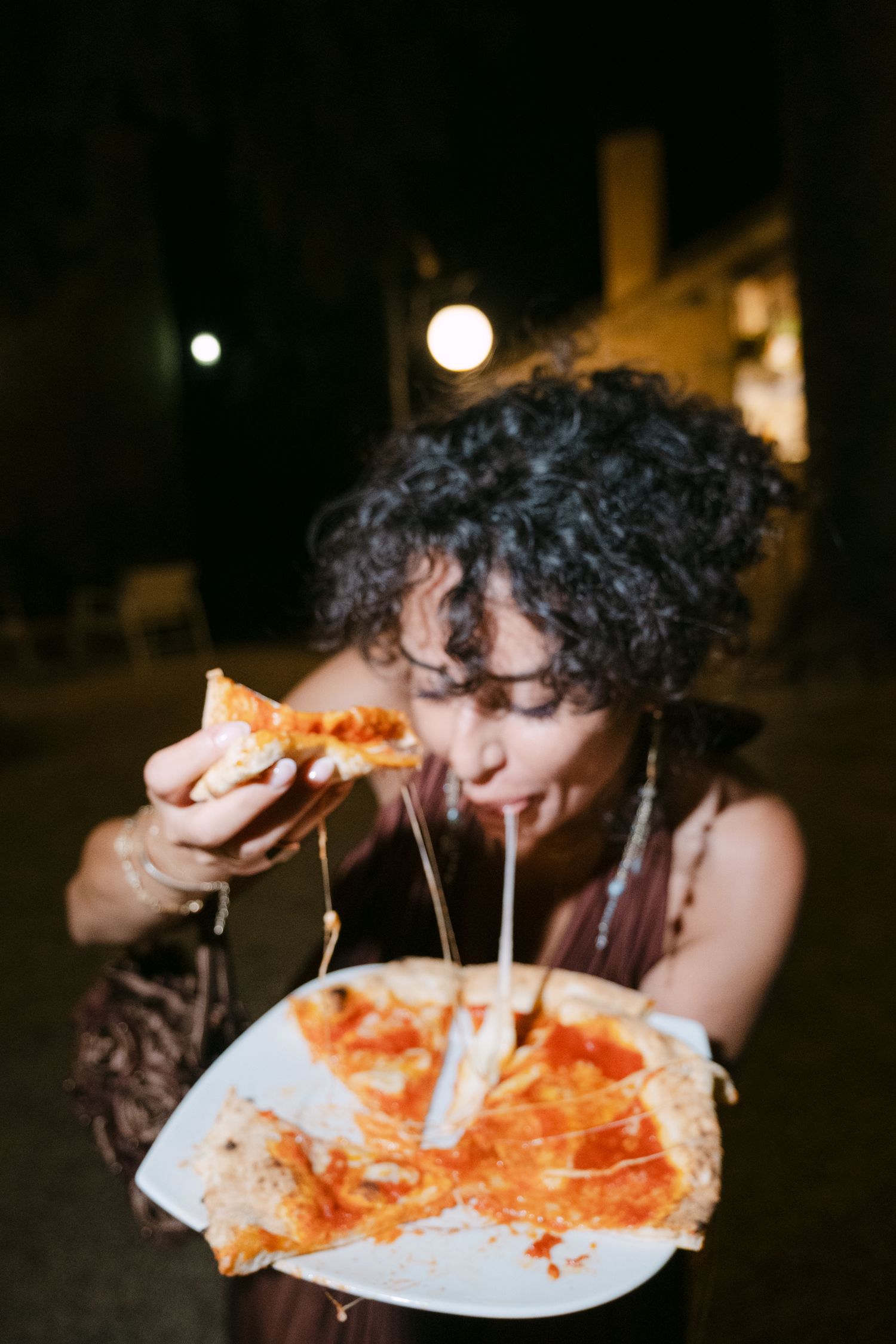 A guest enjoying stretchy cheese pizza at a nighttime wedding reception.