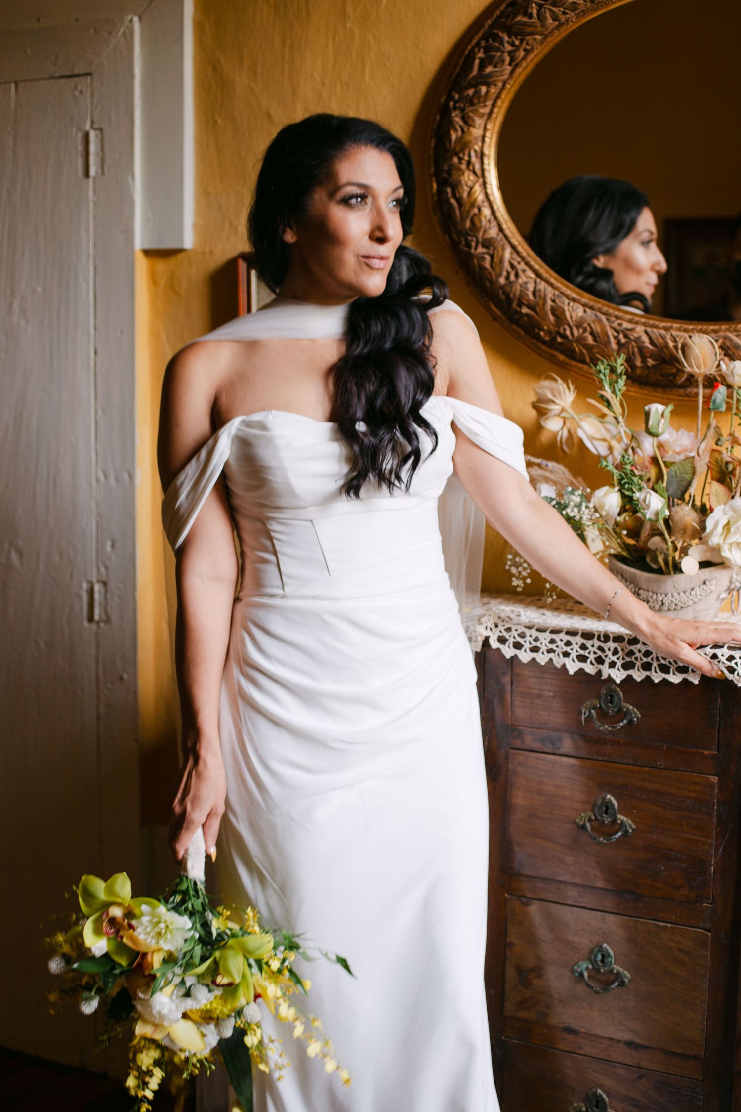 A white wedding dress is photographed against an antique wooden dresser with ornate details.