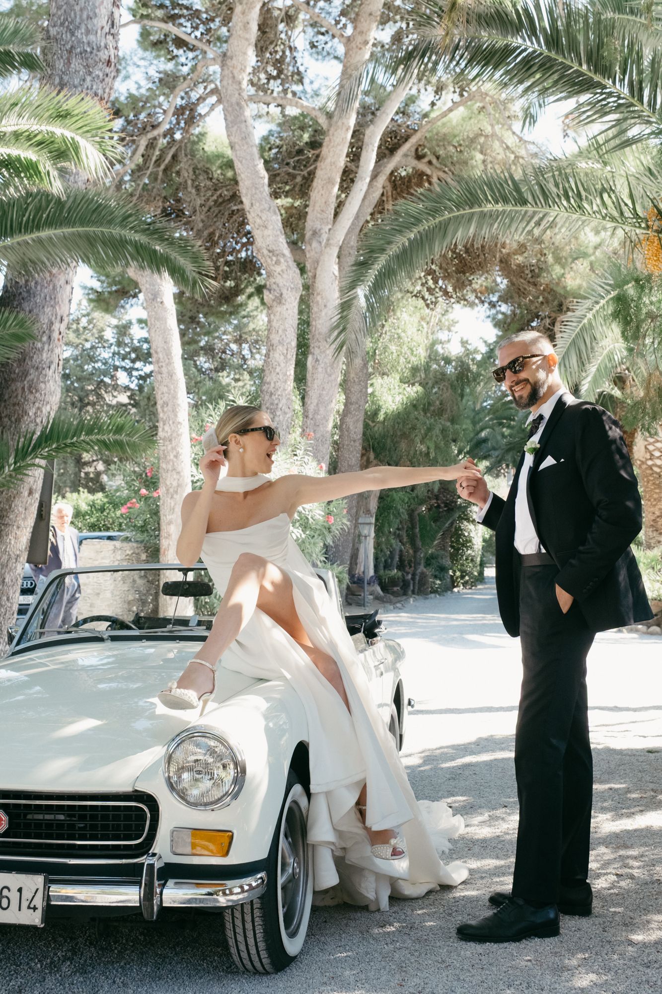 Classic white vintage Mercedes-Benz car parked among palm trees at an outdoor event.