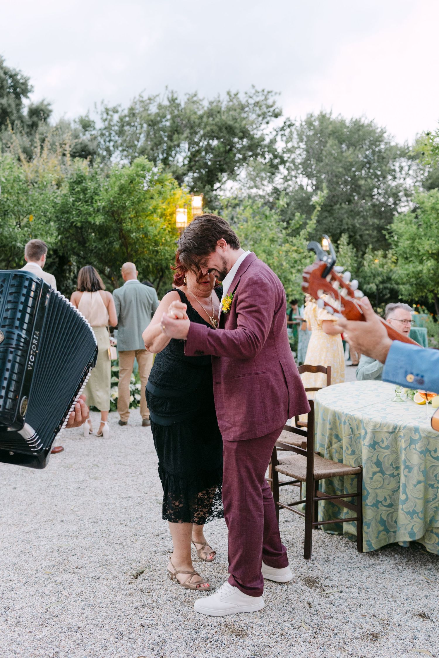 Guests dance at an outdoor wedding reception with an accordion player visible.