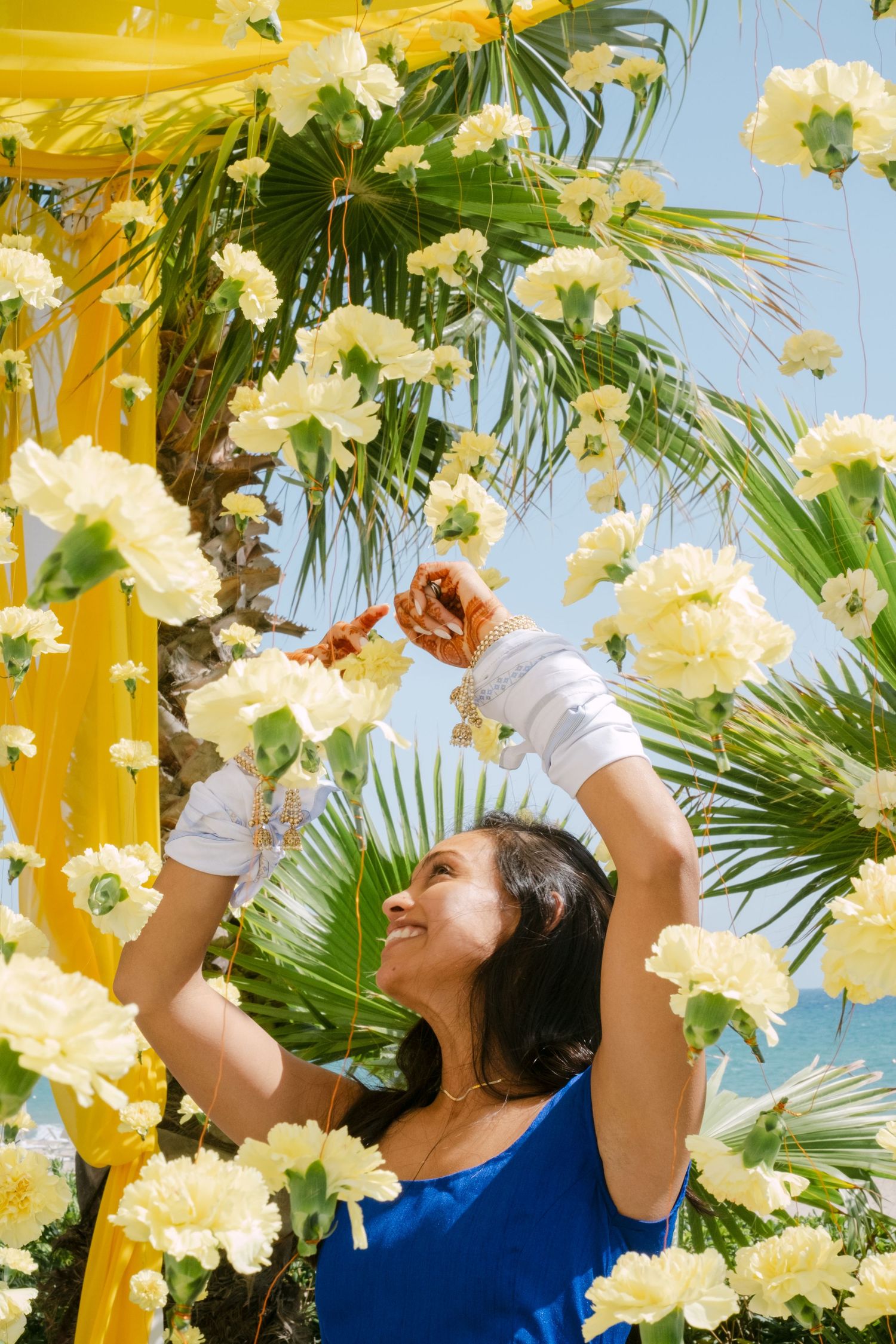 Yellow and cream flowers cascade down with palm fronds against a bright blue sky.