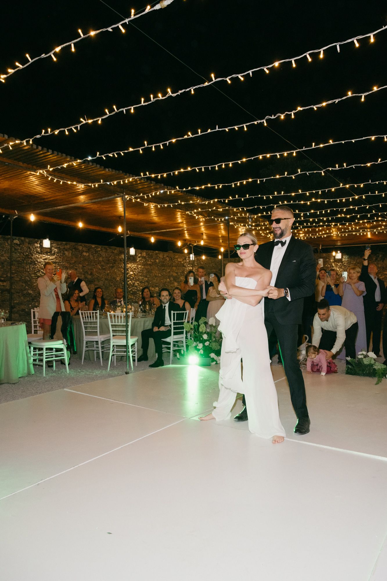 Wedding reception dance floor under twinkling string lights with guests celebrating in an indoor venue.