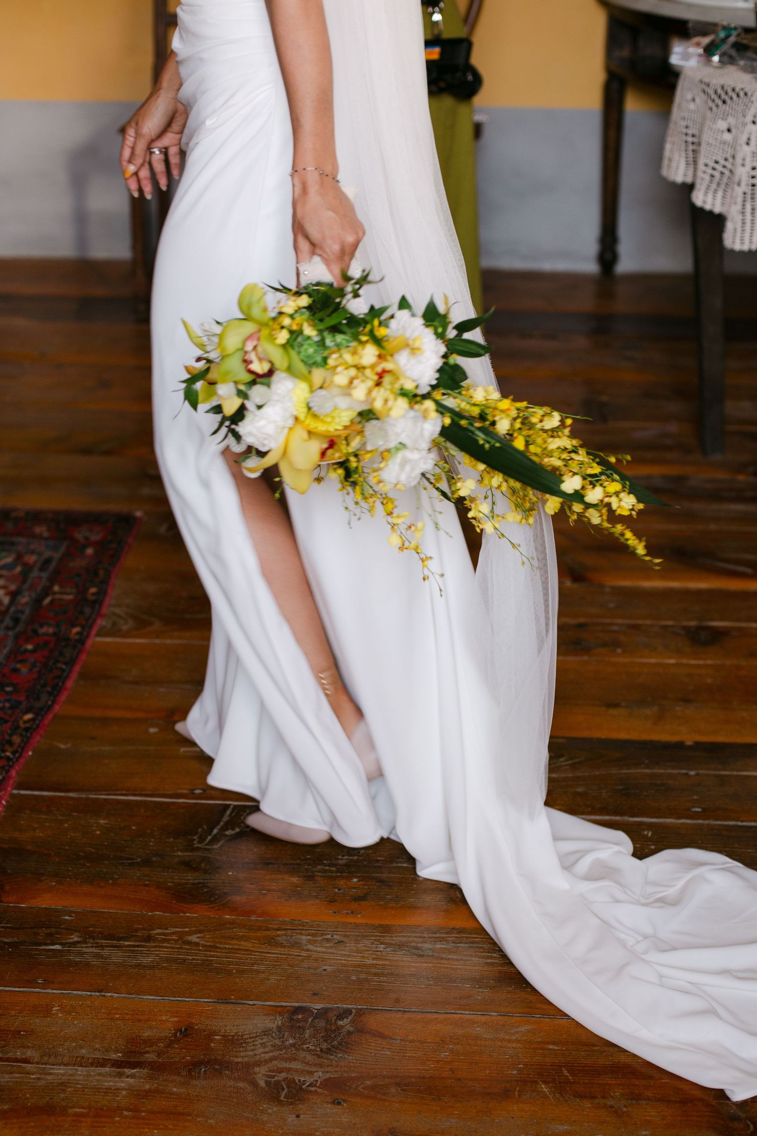 White wedding dress train with yellow floral bouquet on wooden floor.