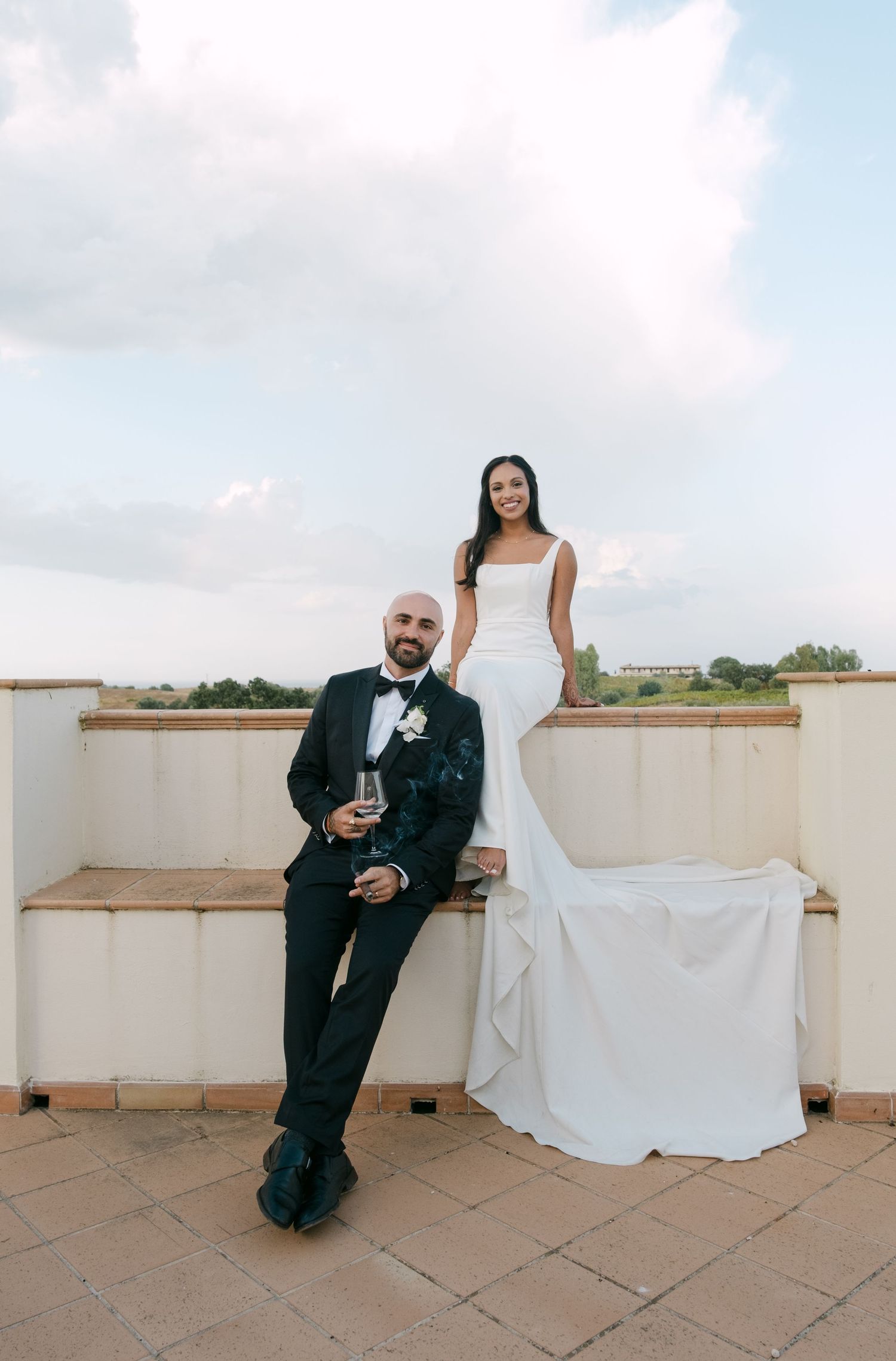 A series of romantic wedding photos showing a couple sitting on a terrace with white walls against a cloudy sky.
