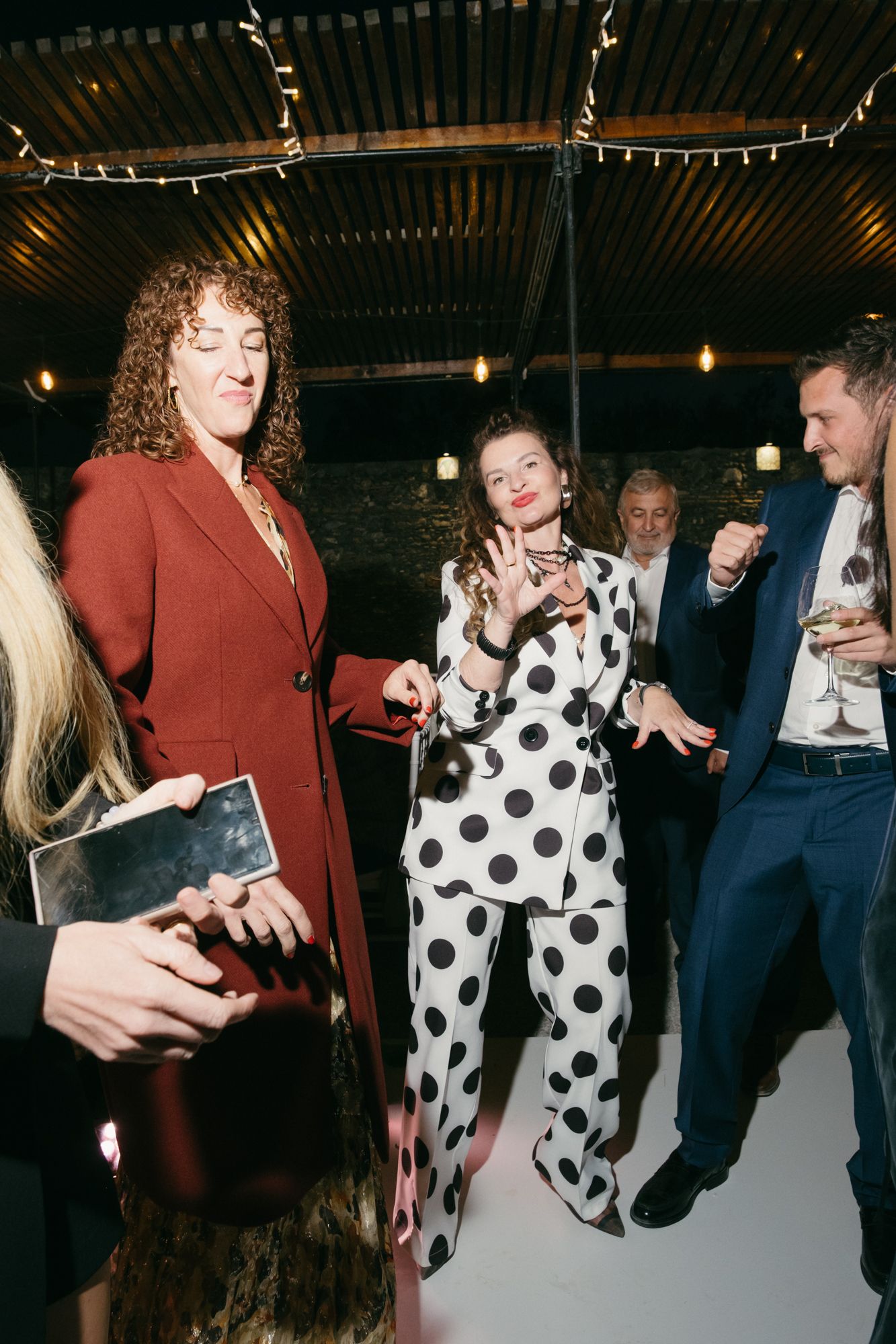 A group of people at a party, with one person wearing a red suit and another in a polka dot jumpsuit.