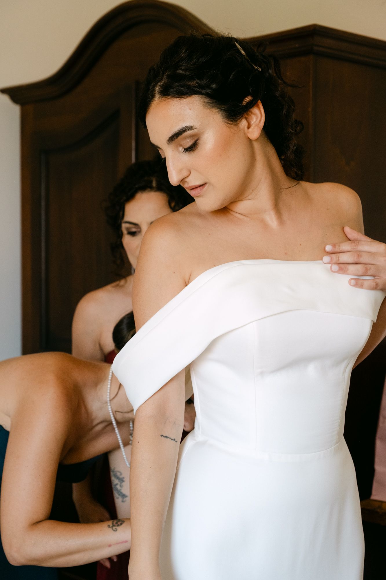 Elegant off-shoulder white wedding dress being adjusted during bridal preparation.