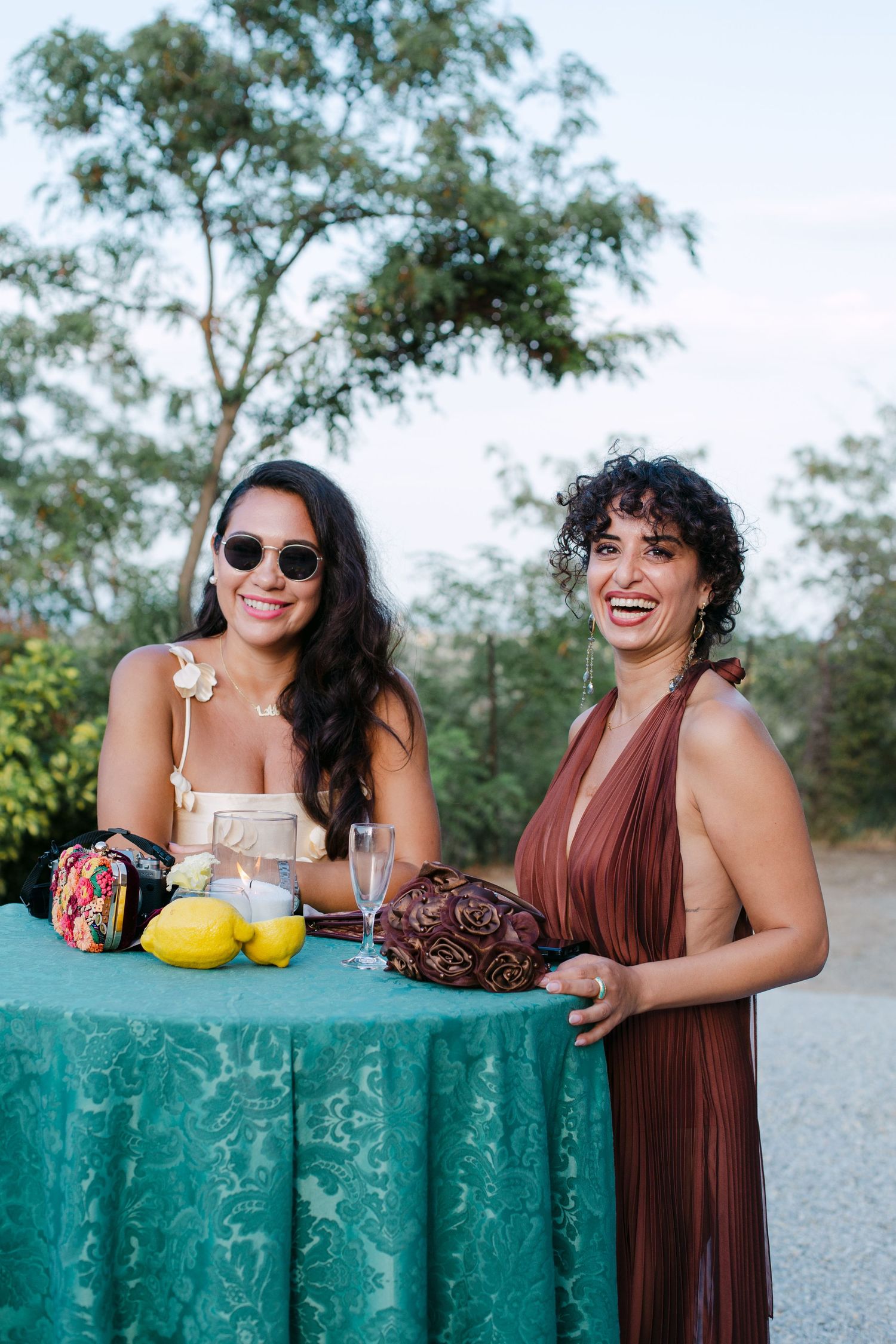 Women in brown dresses pose playfully behind turquoise wall outdoors.