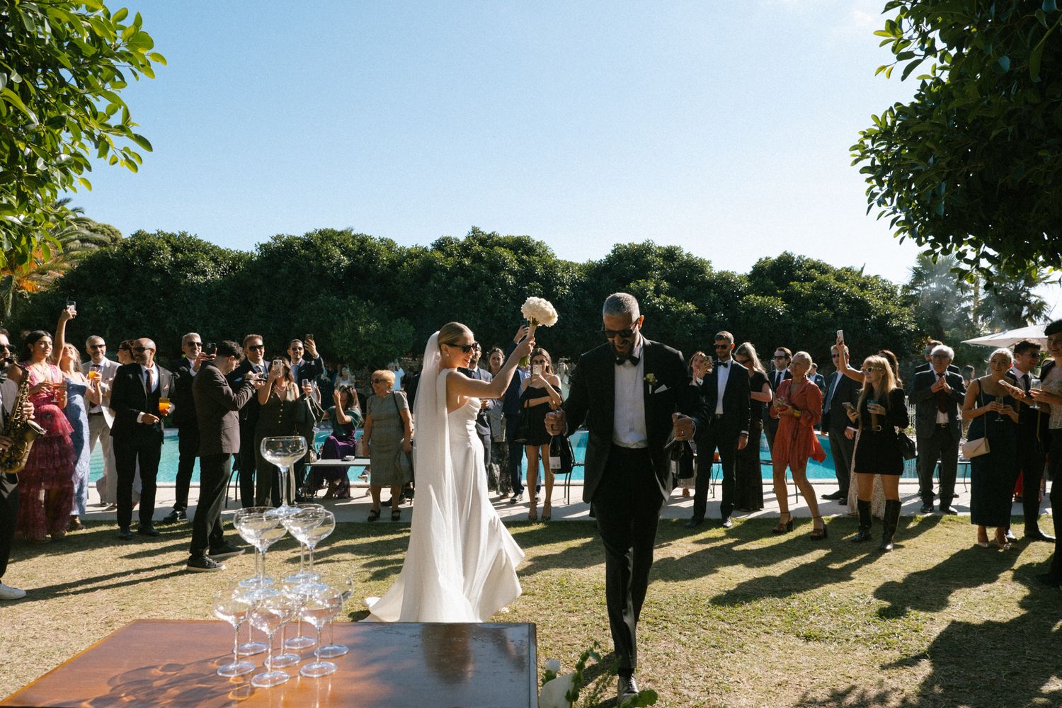 Outdoor wedding ceremony gathering with guests standing in a garden setting.