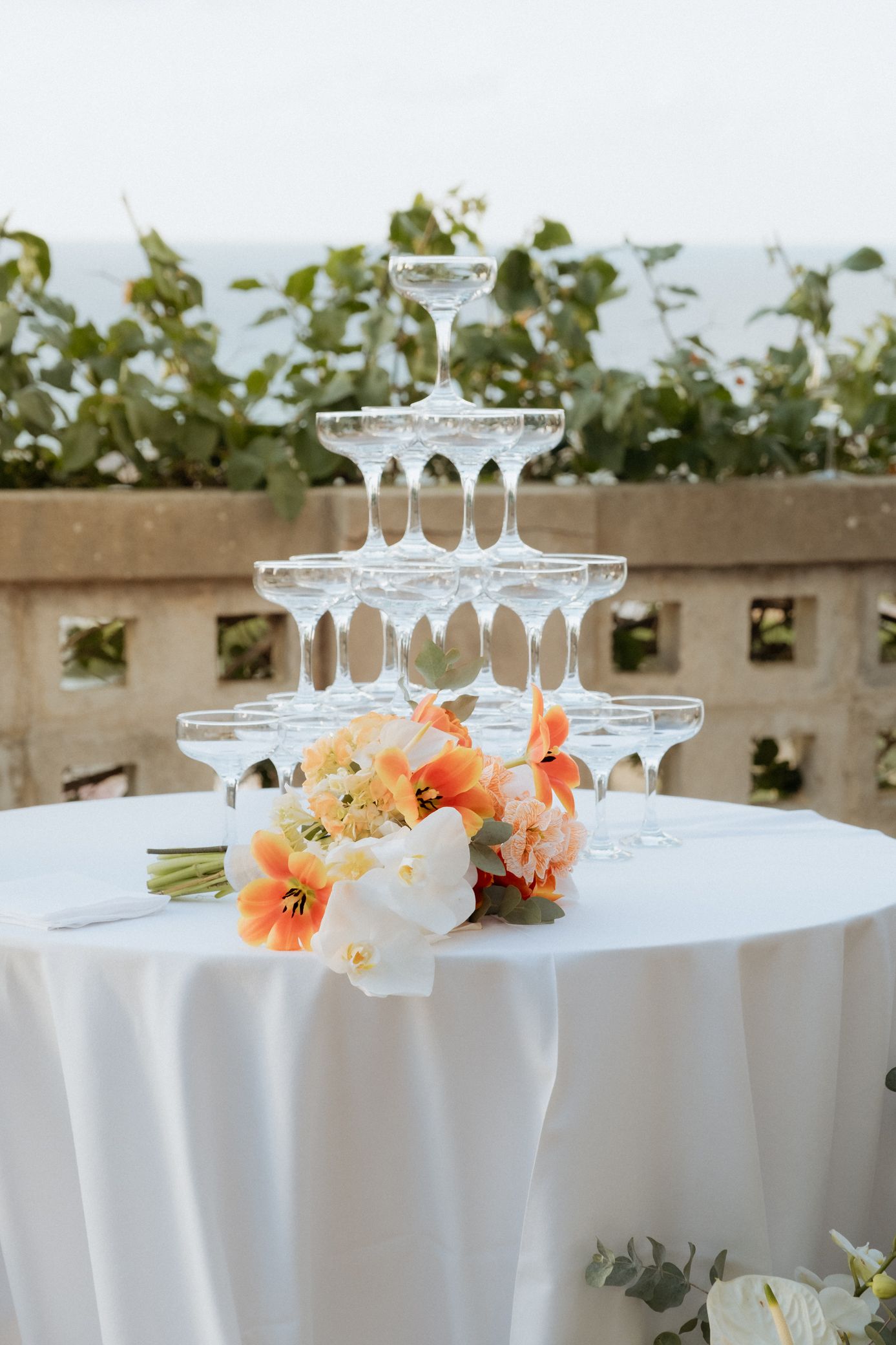 White tablecloth covered tables with stacked champagne glasses and coral-colored floral centerpieces for a wedding reception.