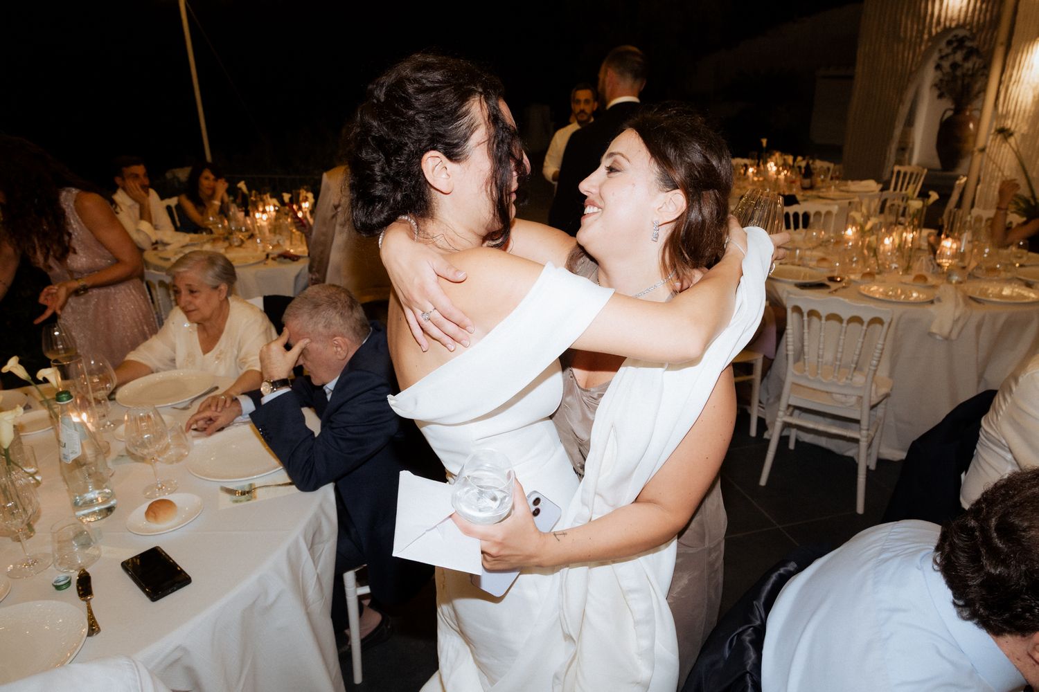 Two people in white dresses dancing and laughing at wedding reception.