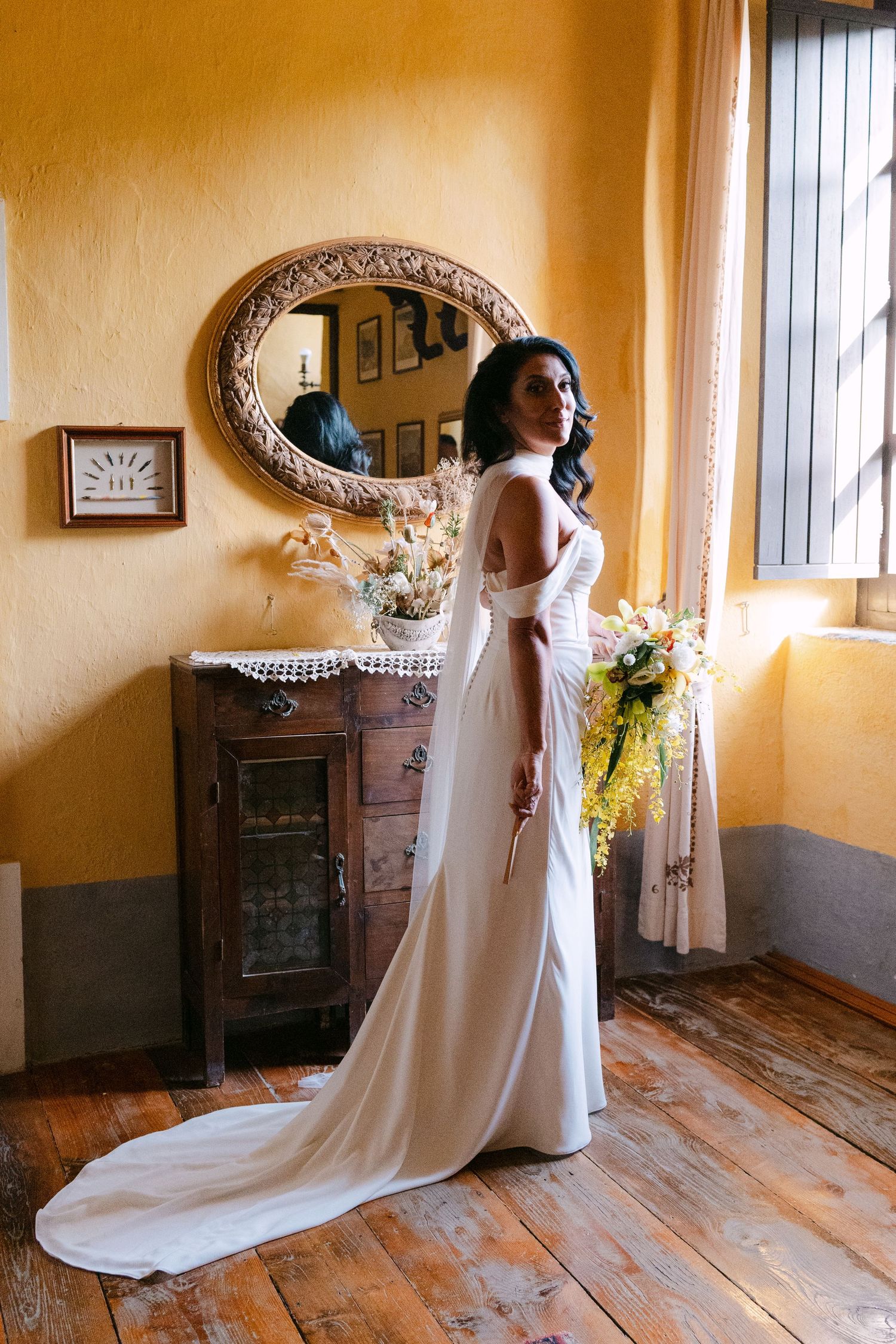 An elegant white wedding gown flows gracefully in a vintage-styled room with warm yellow walls.