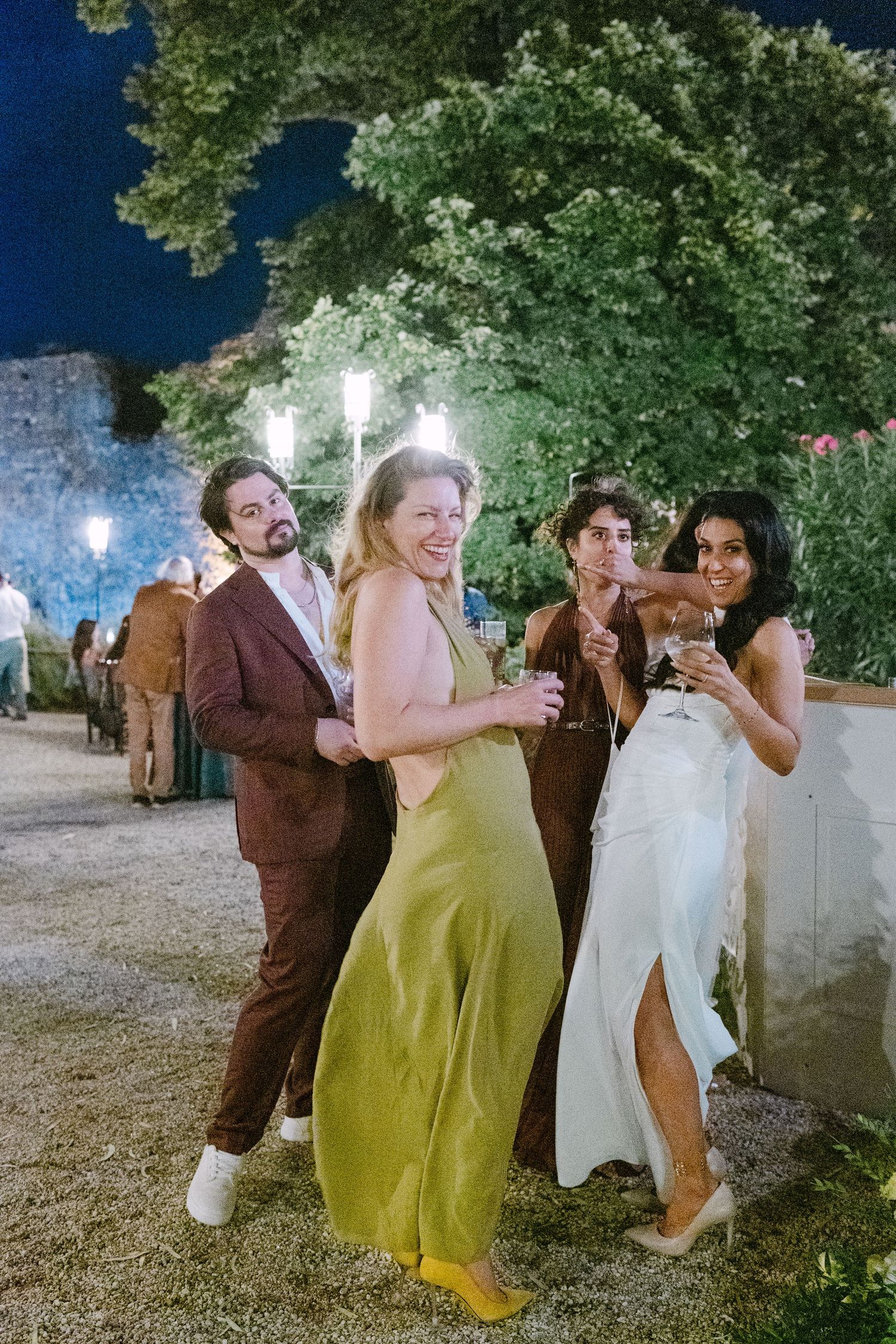 Wedding guests dance and celebrate outdoors at night under string lights and trees.