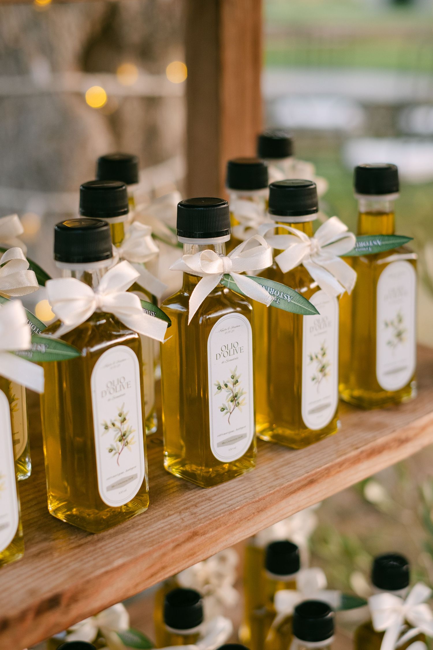 Small bottles of olive oil with white ribbons arranged in a row as wedding favors on a wooden shelf.
