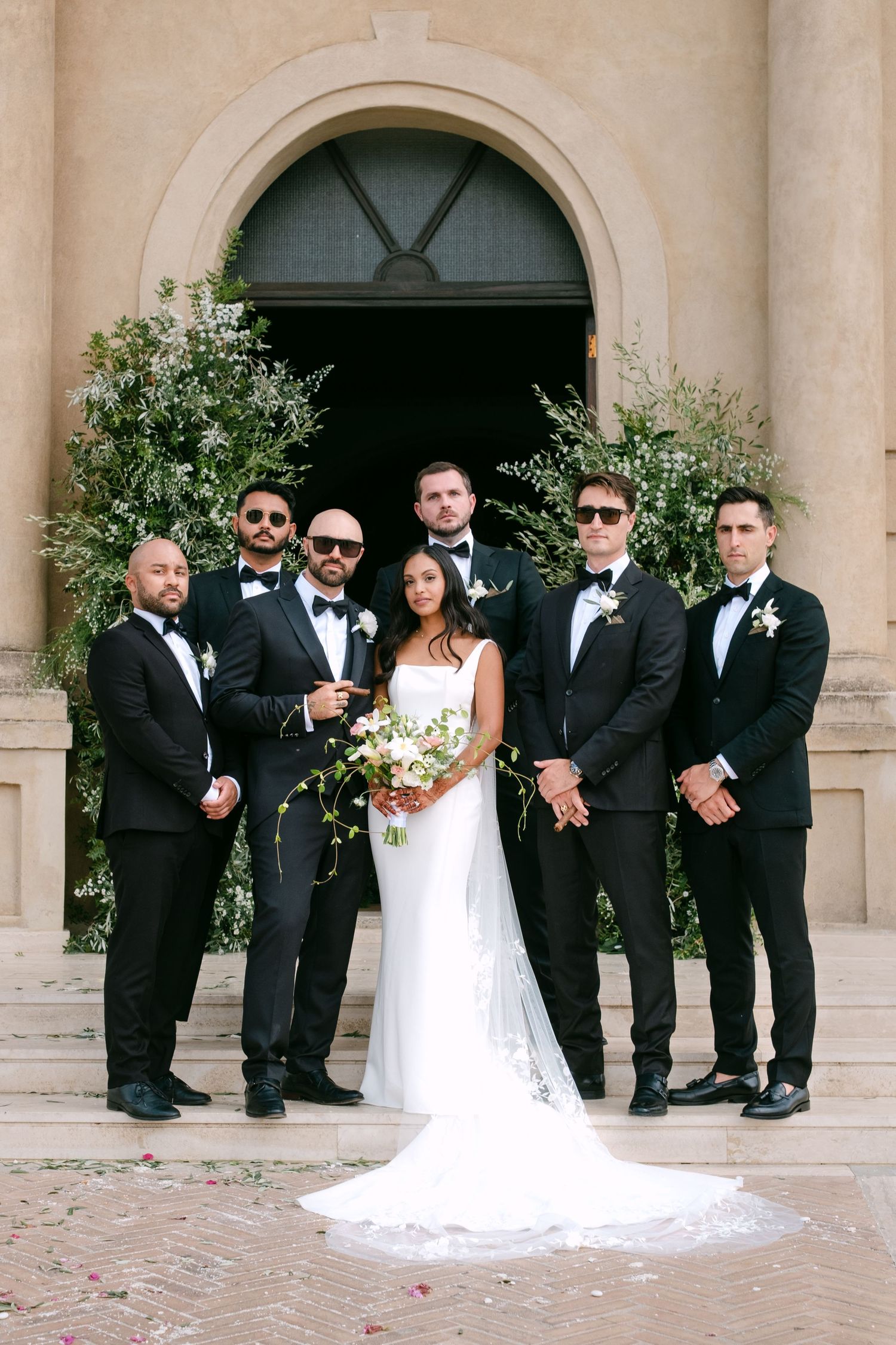 Wedding party in formal black suits and white dress posing on church steps.