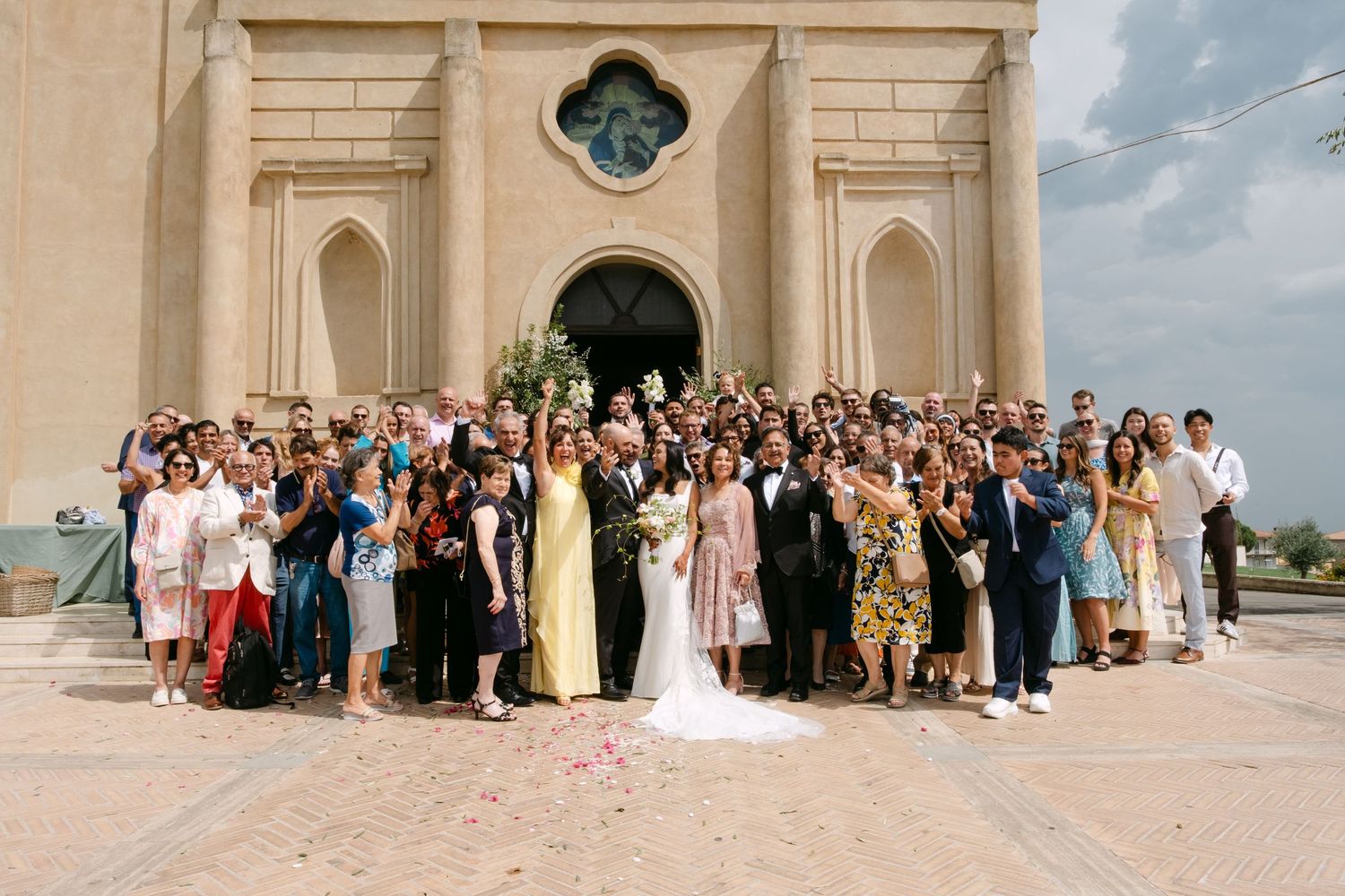 Large wedding group portrait taken outside a classic stone building with arched architecture.