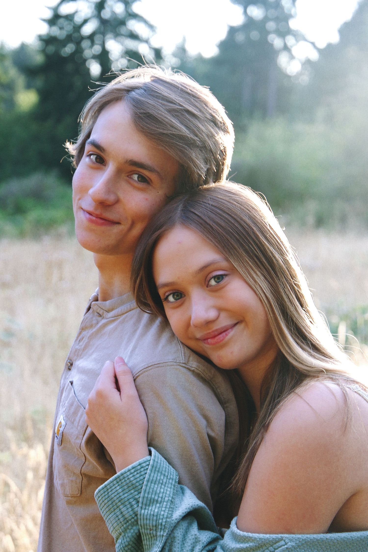 A couple embraces in a sun-lit field of tall grass during a romantic outdoor photoshoot.