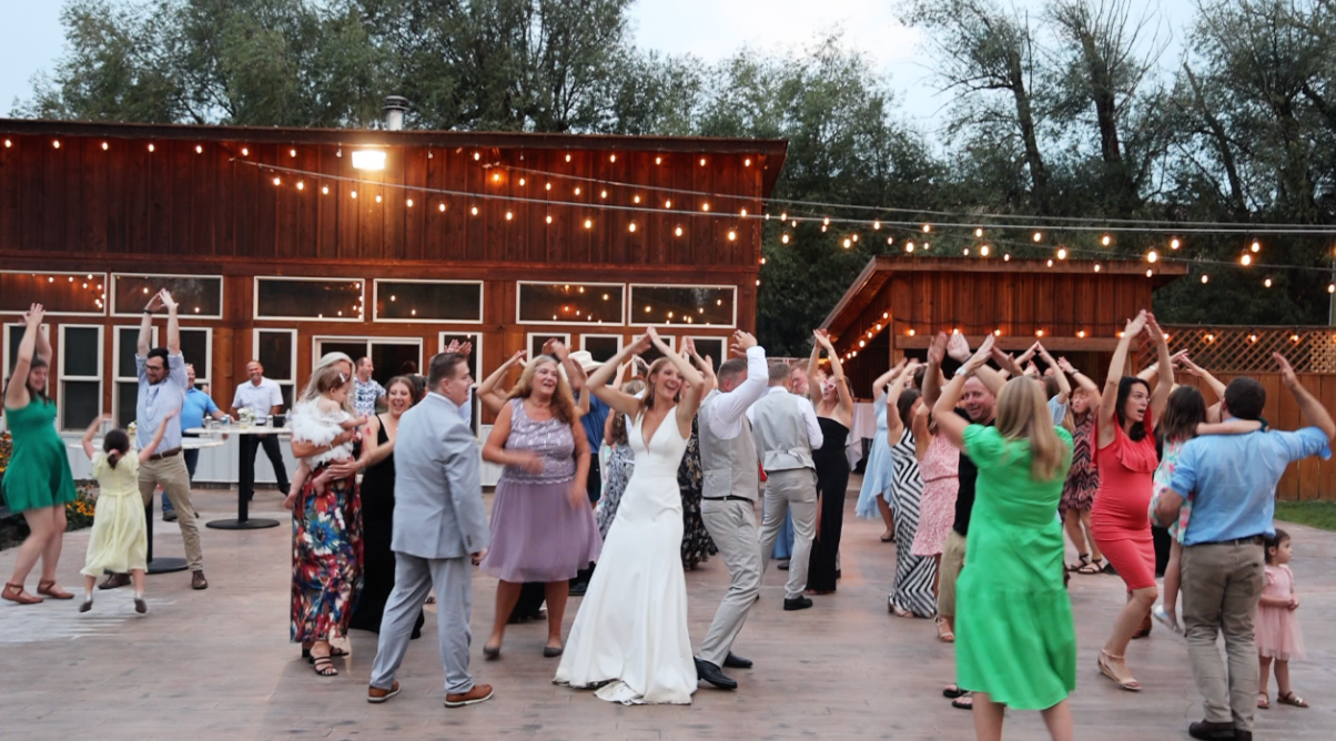 Outdoor wedding reception with string lights and dancing guests at dusk.