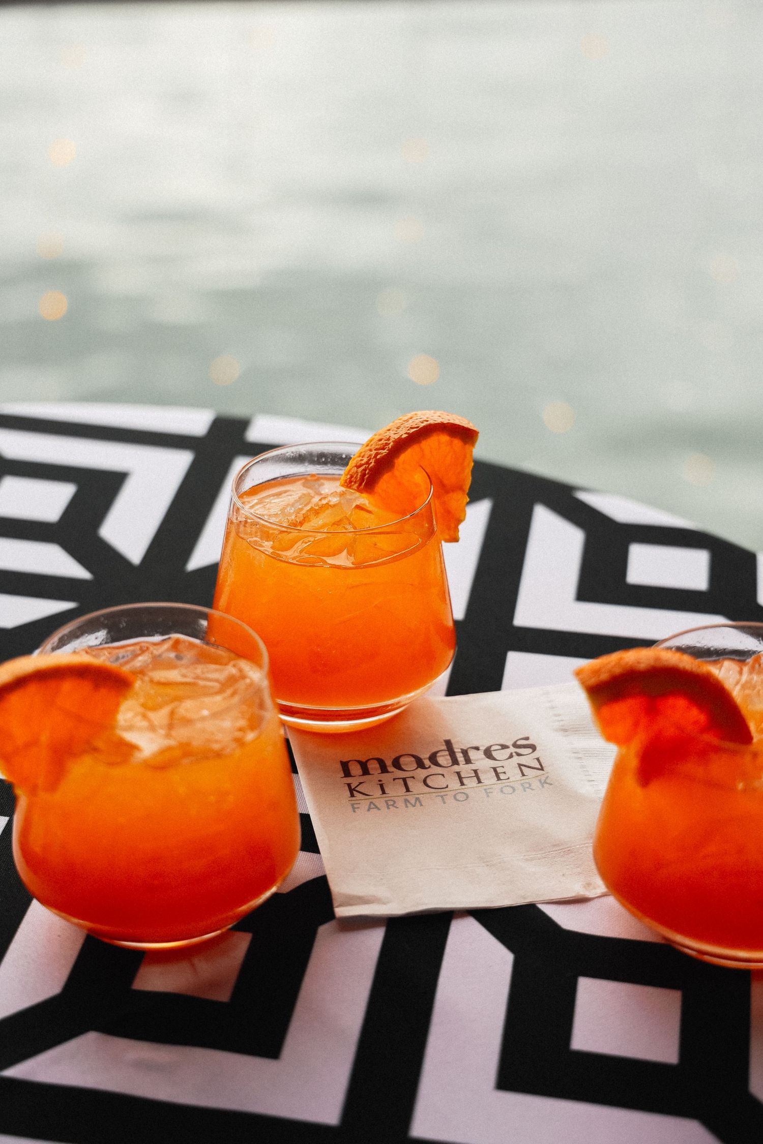 Three bright orange cocktails with citrus garnish on geometric patterned table.