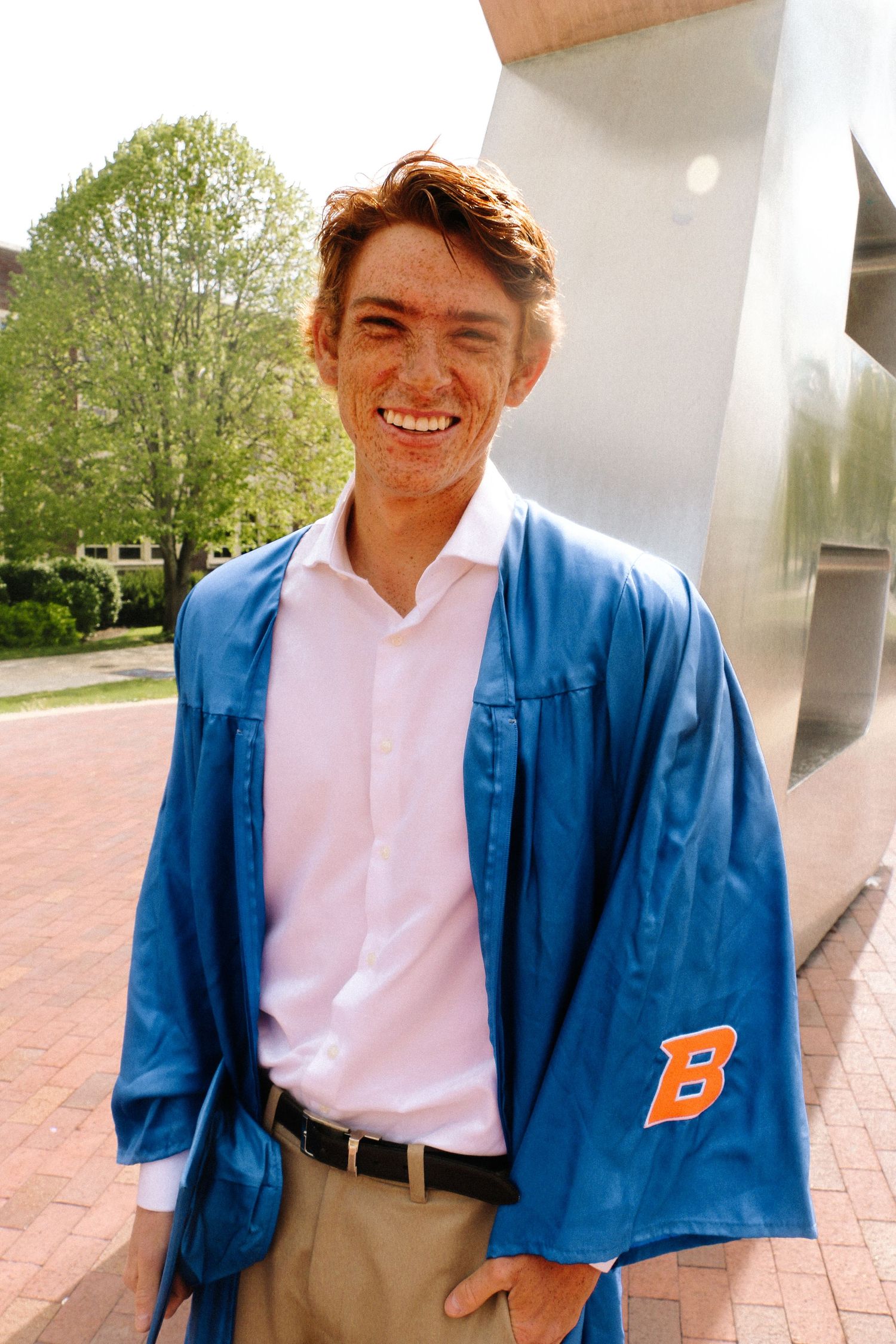 Person wearing a blue varsity jacket and white shirt poses in a series of candid shots on a brick walkway.