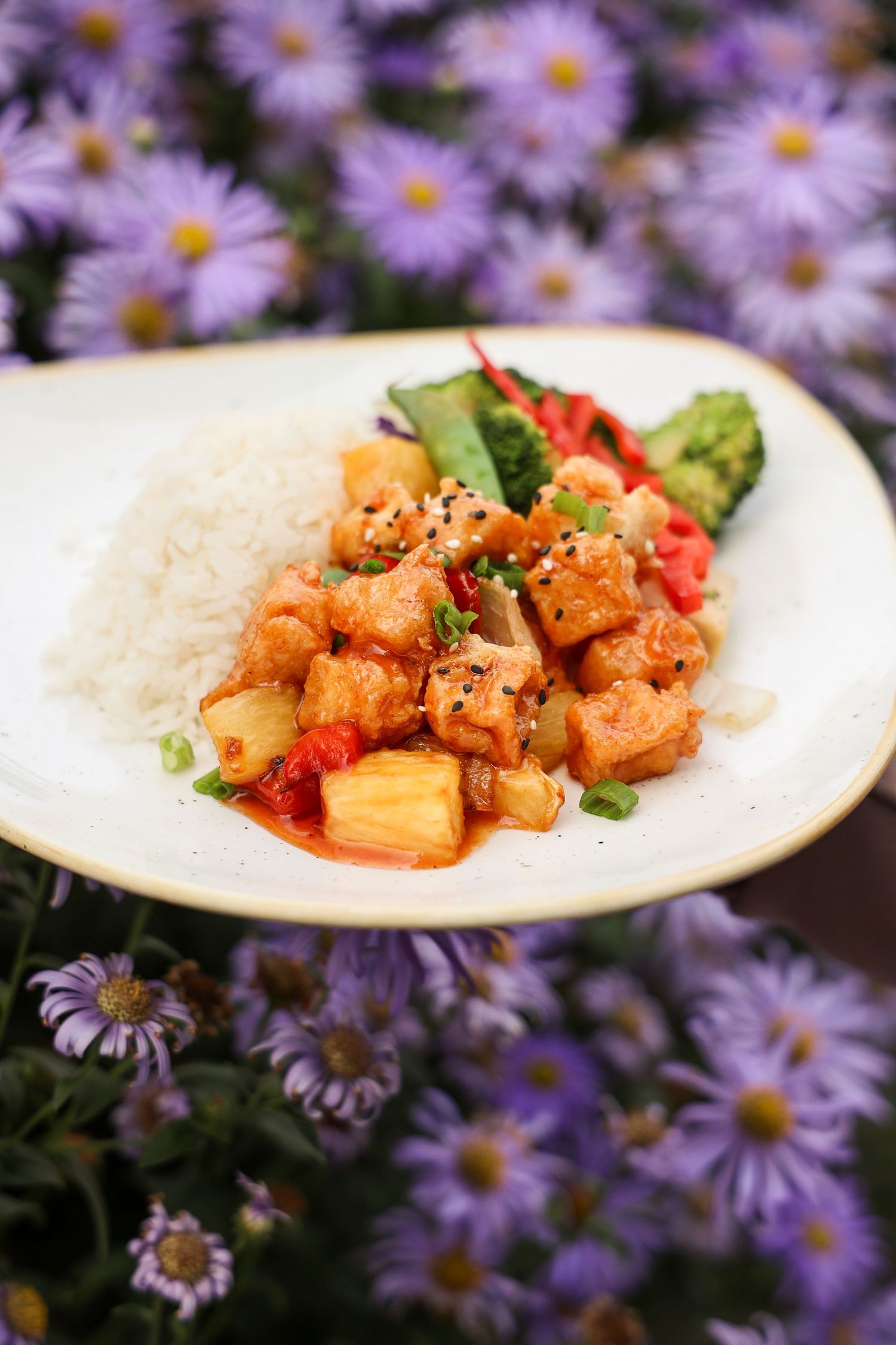 Spicy shrimp dish plated on white dishes with purple aster flowers in background.