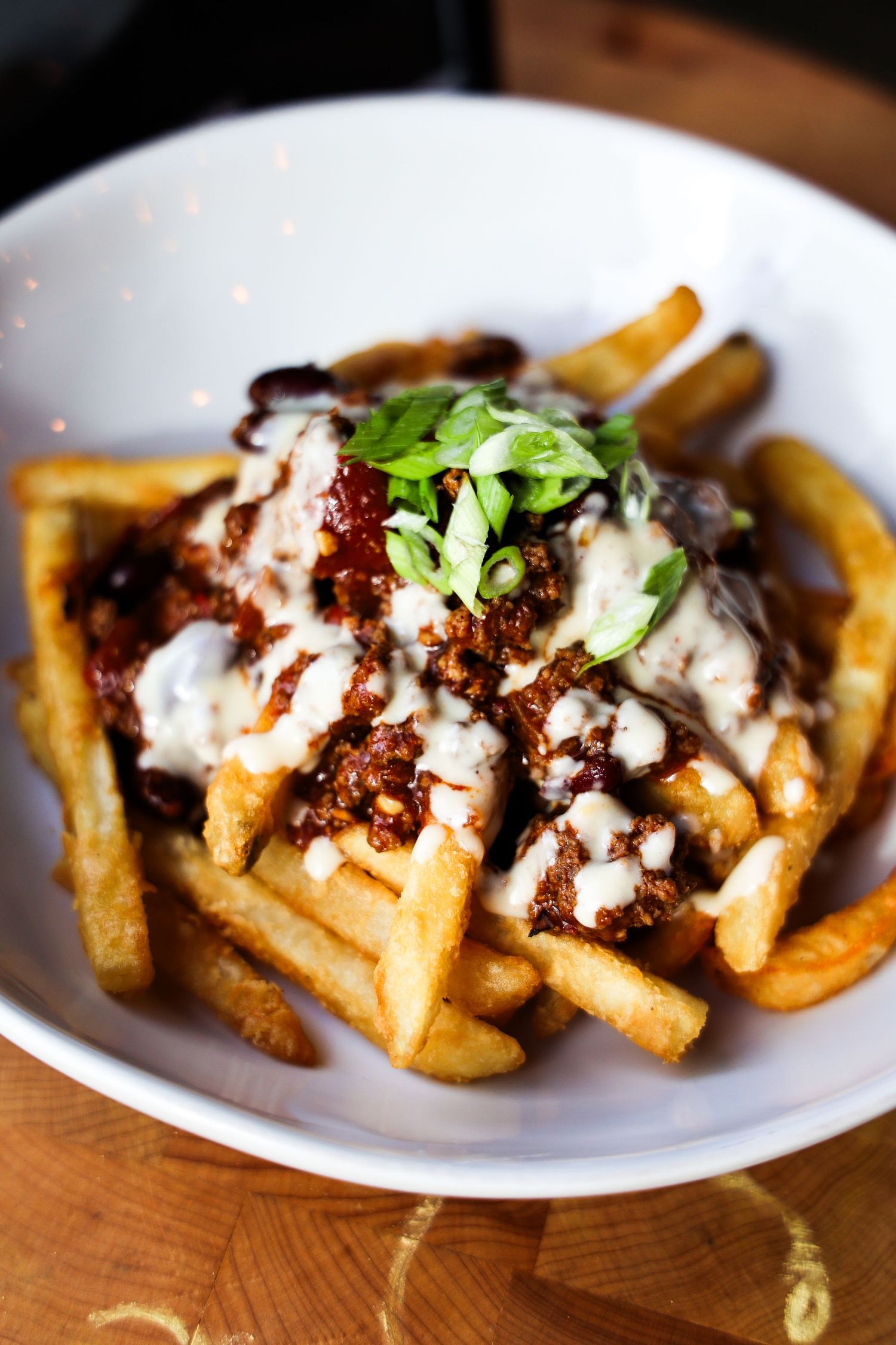 Loaded french fries topped with meat sauce, creamy white sauce, and fresh herbs served in a white bowl.